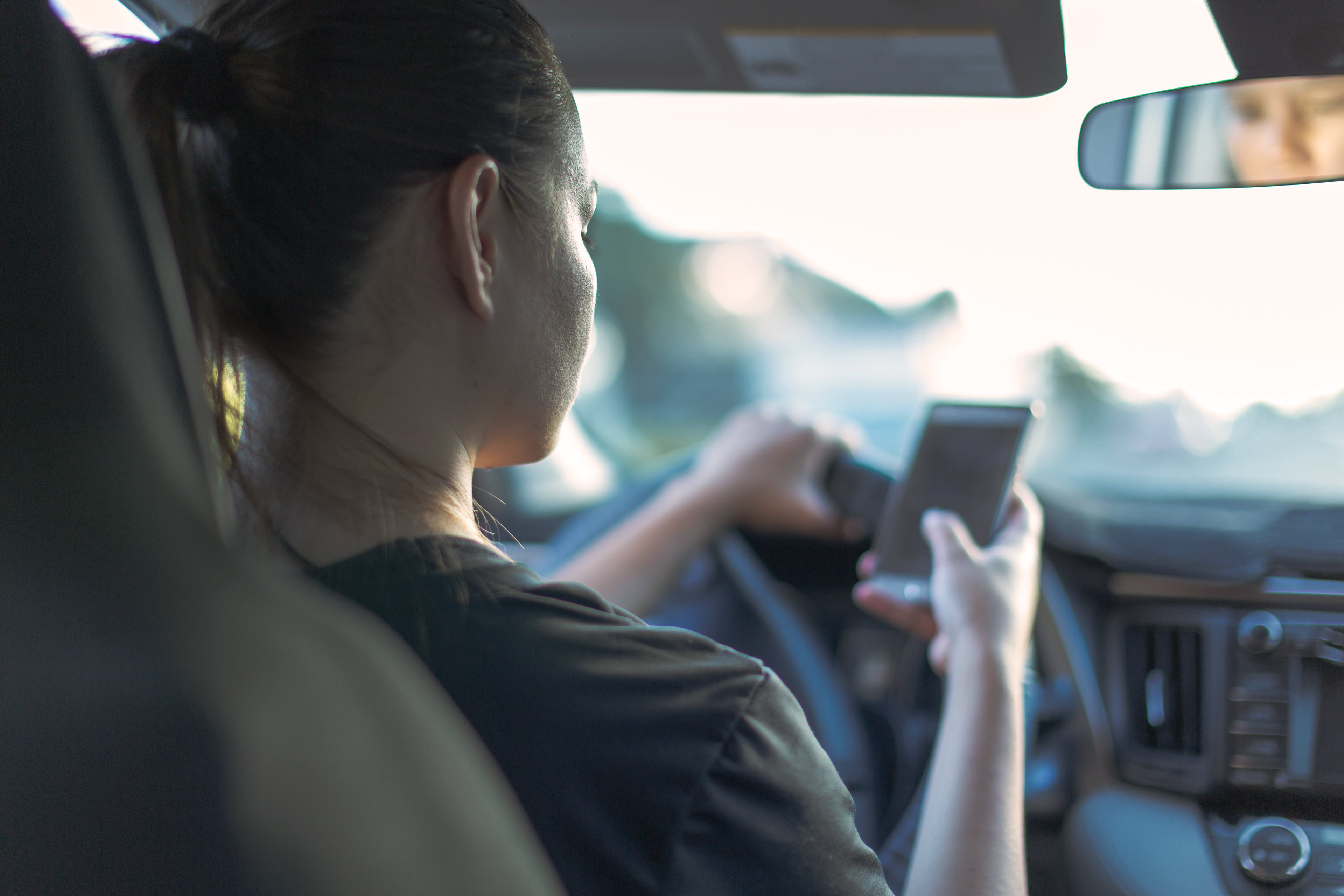 A photo shows a woman in the driver's seat of a car using her phone while driving.