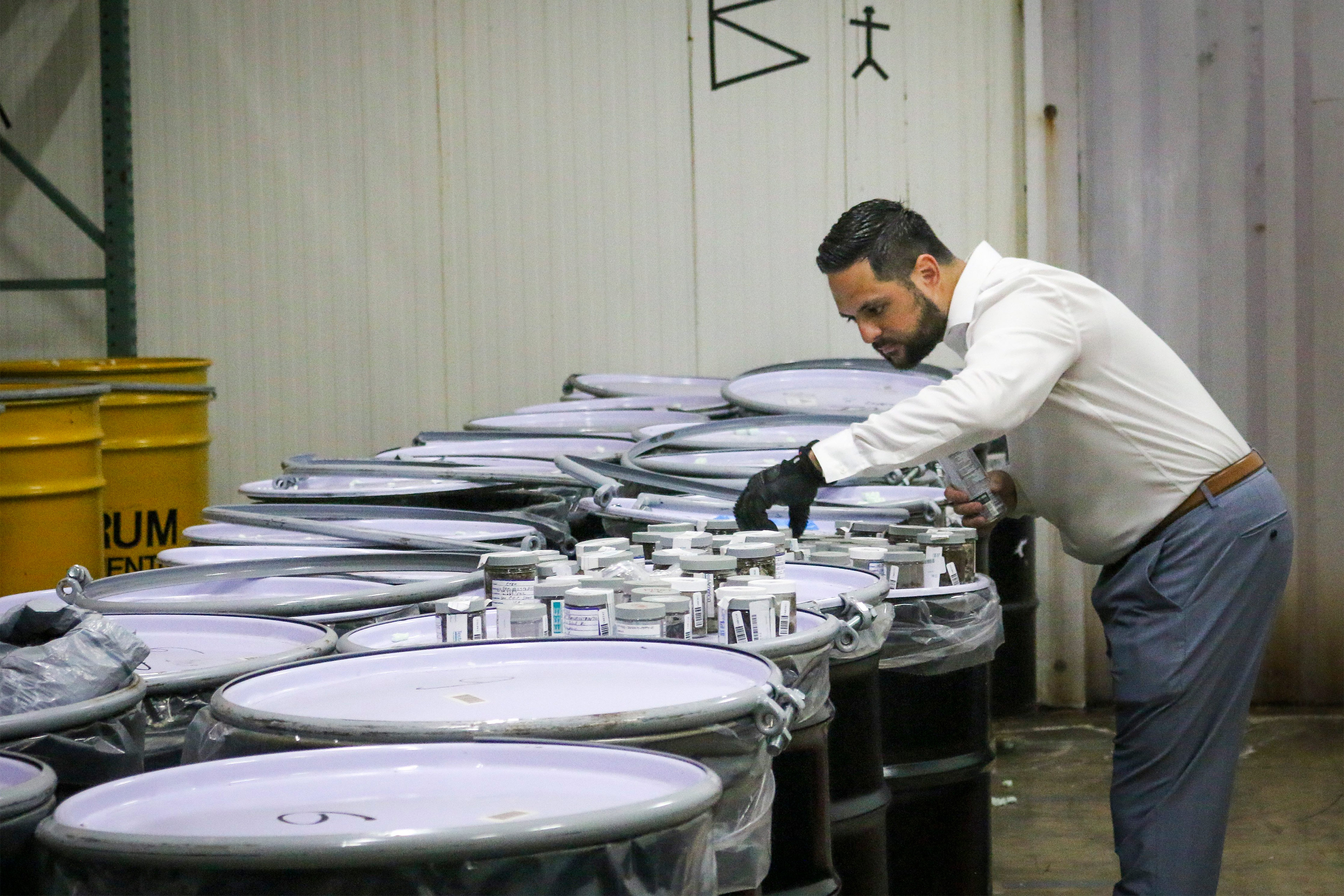 A photo shows a man wearing protective gloves examining the contents of a jar inside a storage facility.