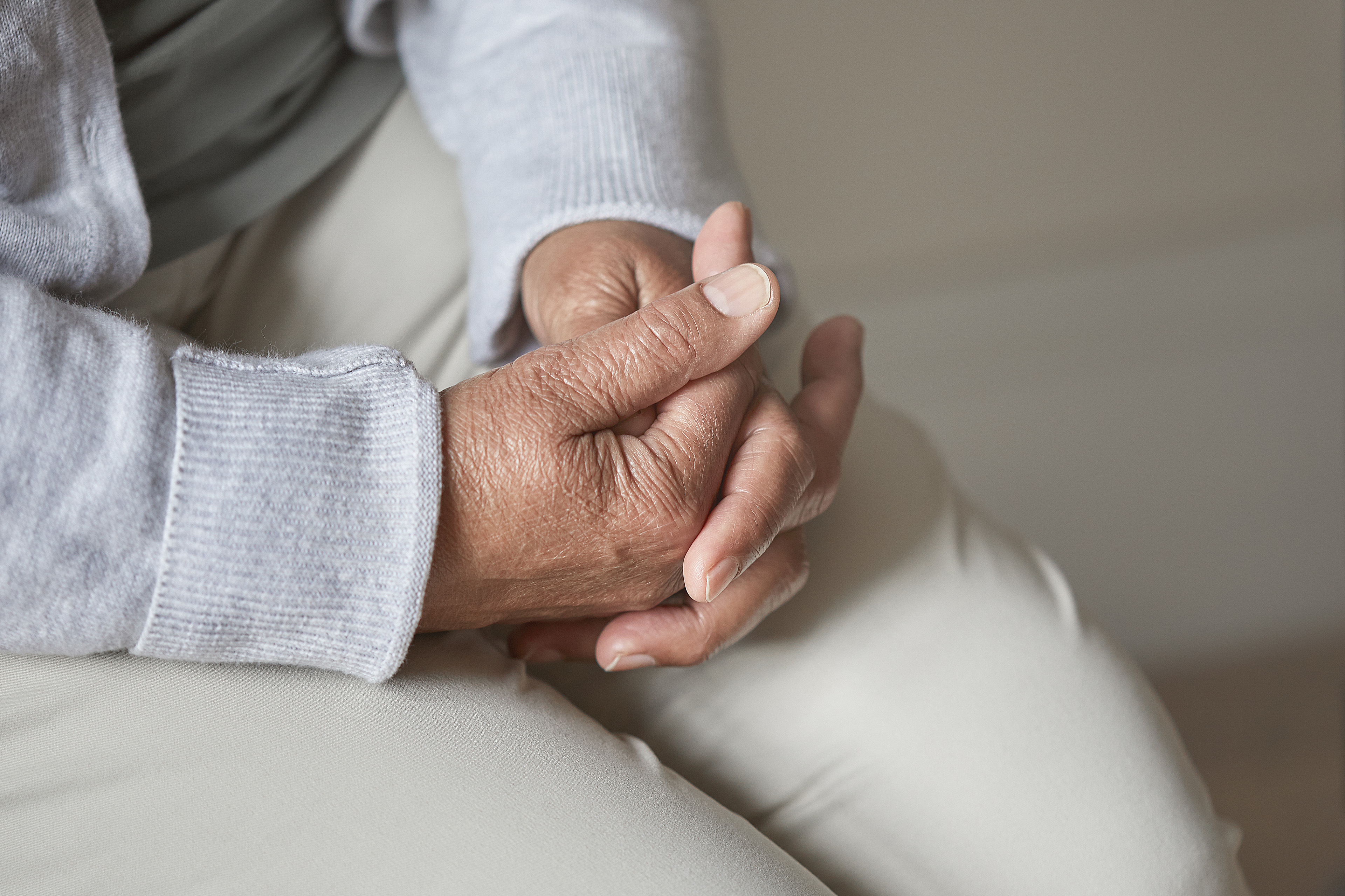 Cropped shot of a senior person sitting with her hands clasped.