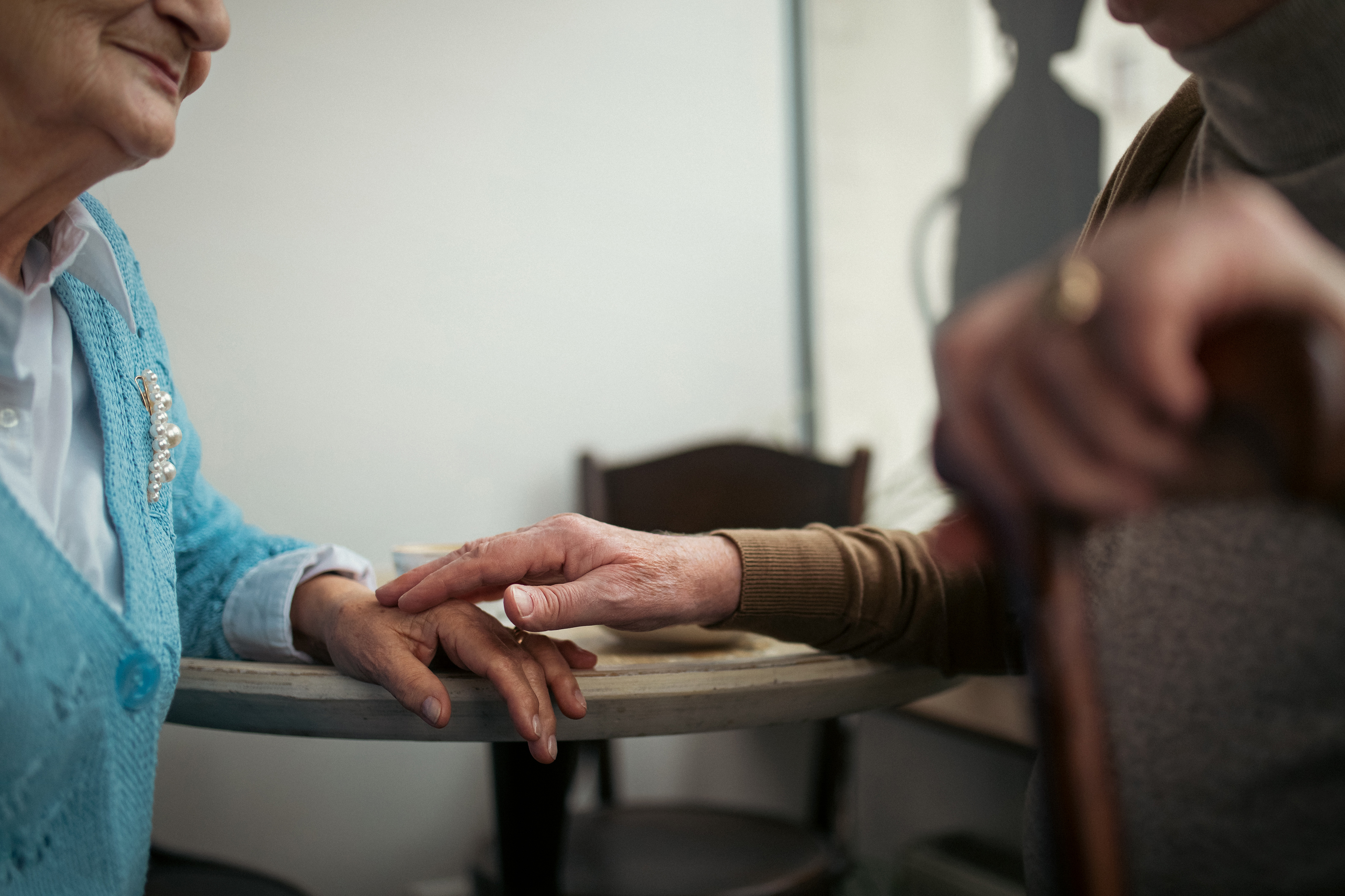 Midsection of older man touching older woman's hand in café.