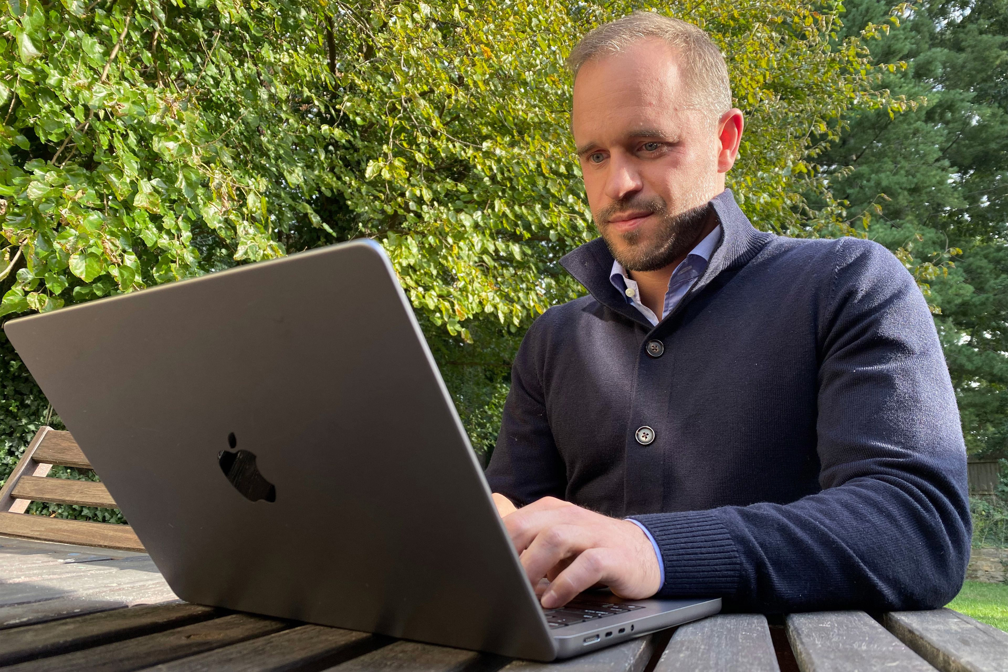 A photo shows a man typing on a laptop outside.
