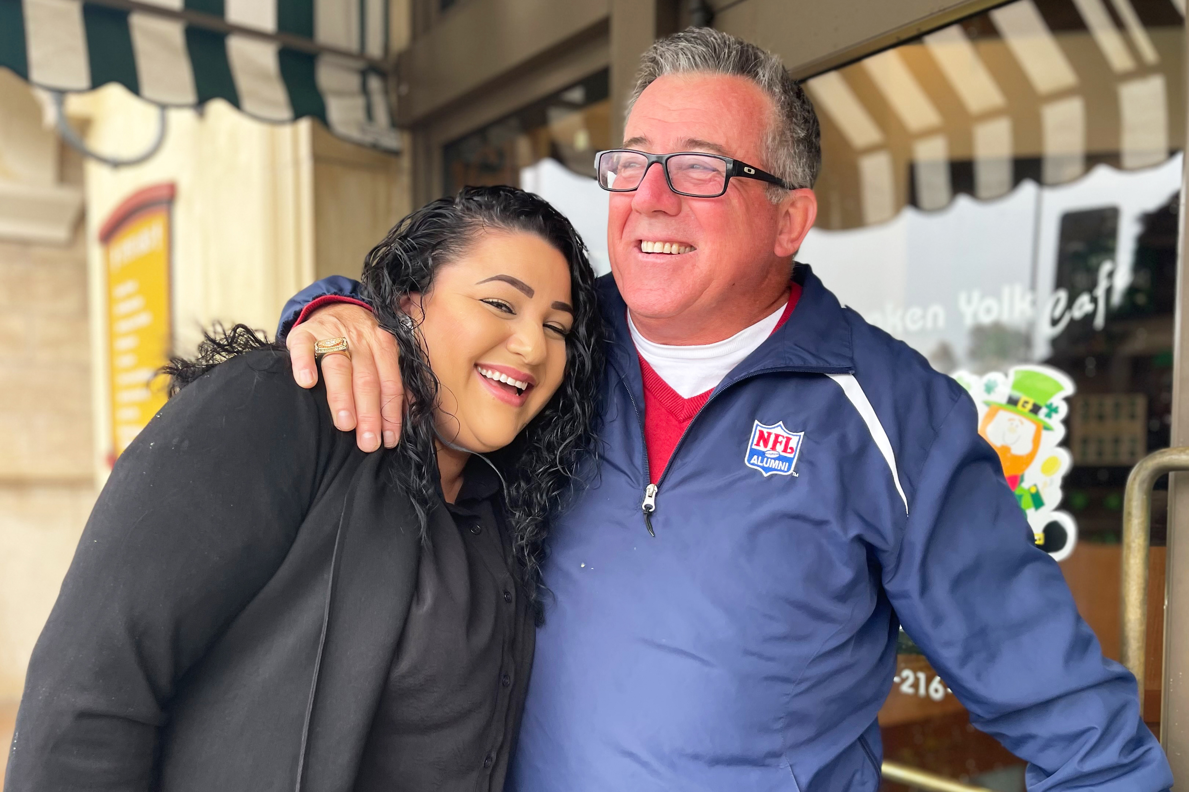 A photo of a man and a woman hugging outside of a restaurant.