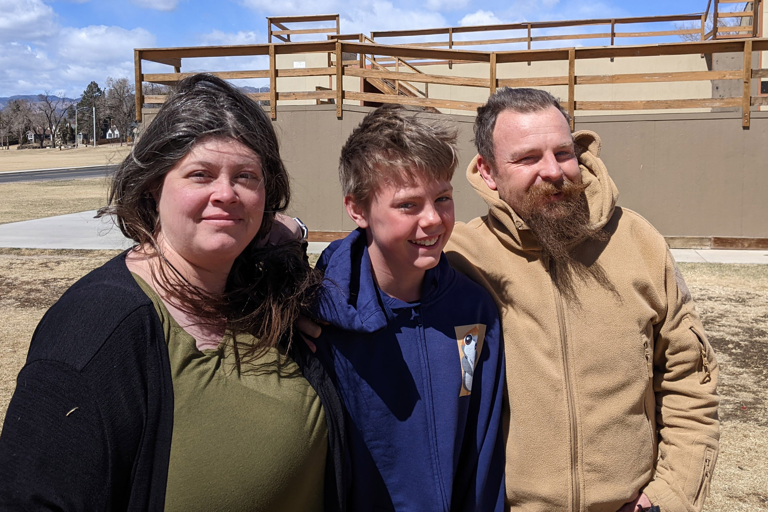 A photo of a young boy posing for a photo with his mother and father outside.
