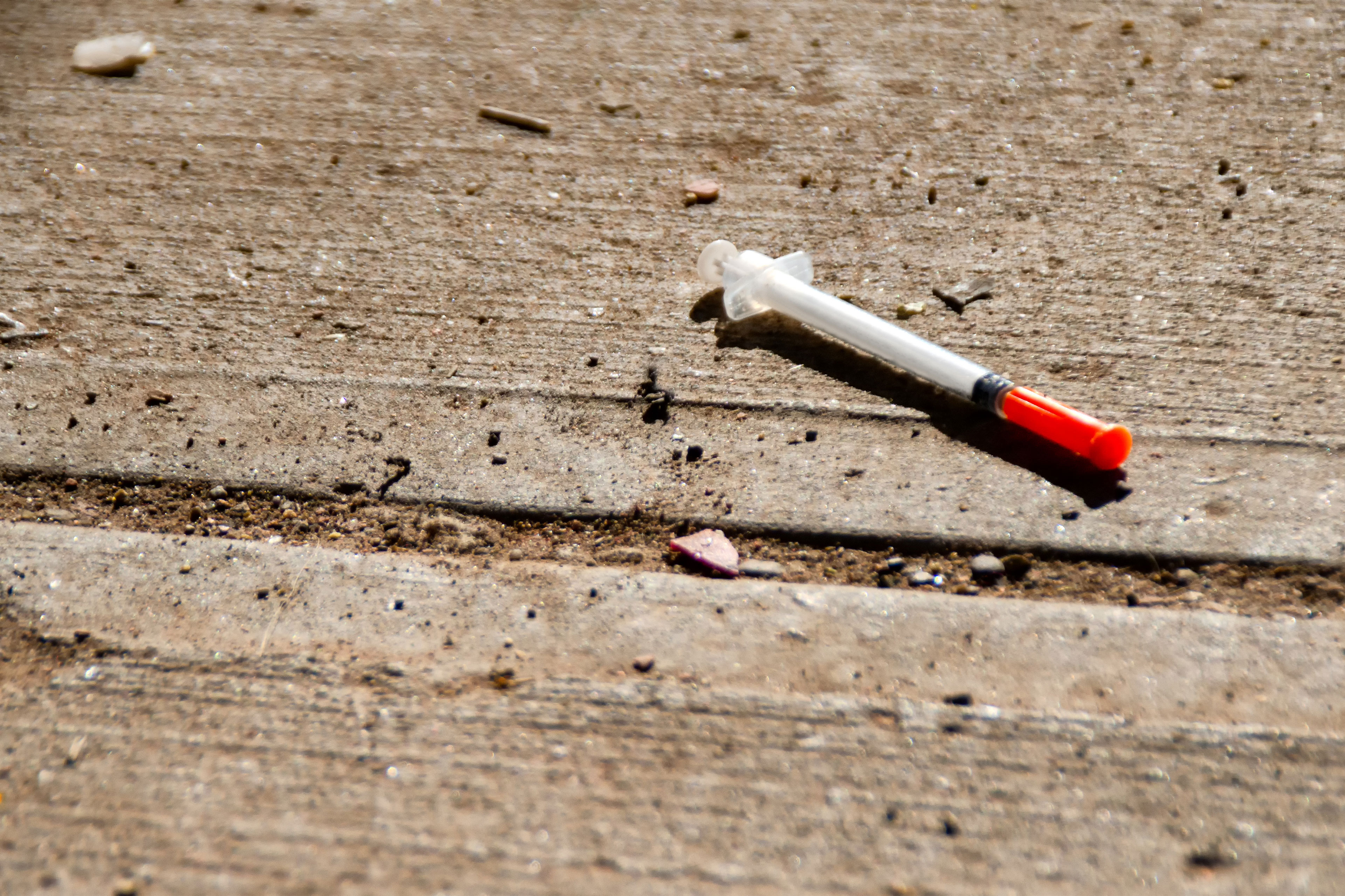 A photo of a discarded needle on the sidewalk.