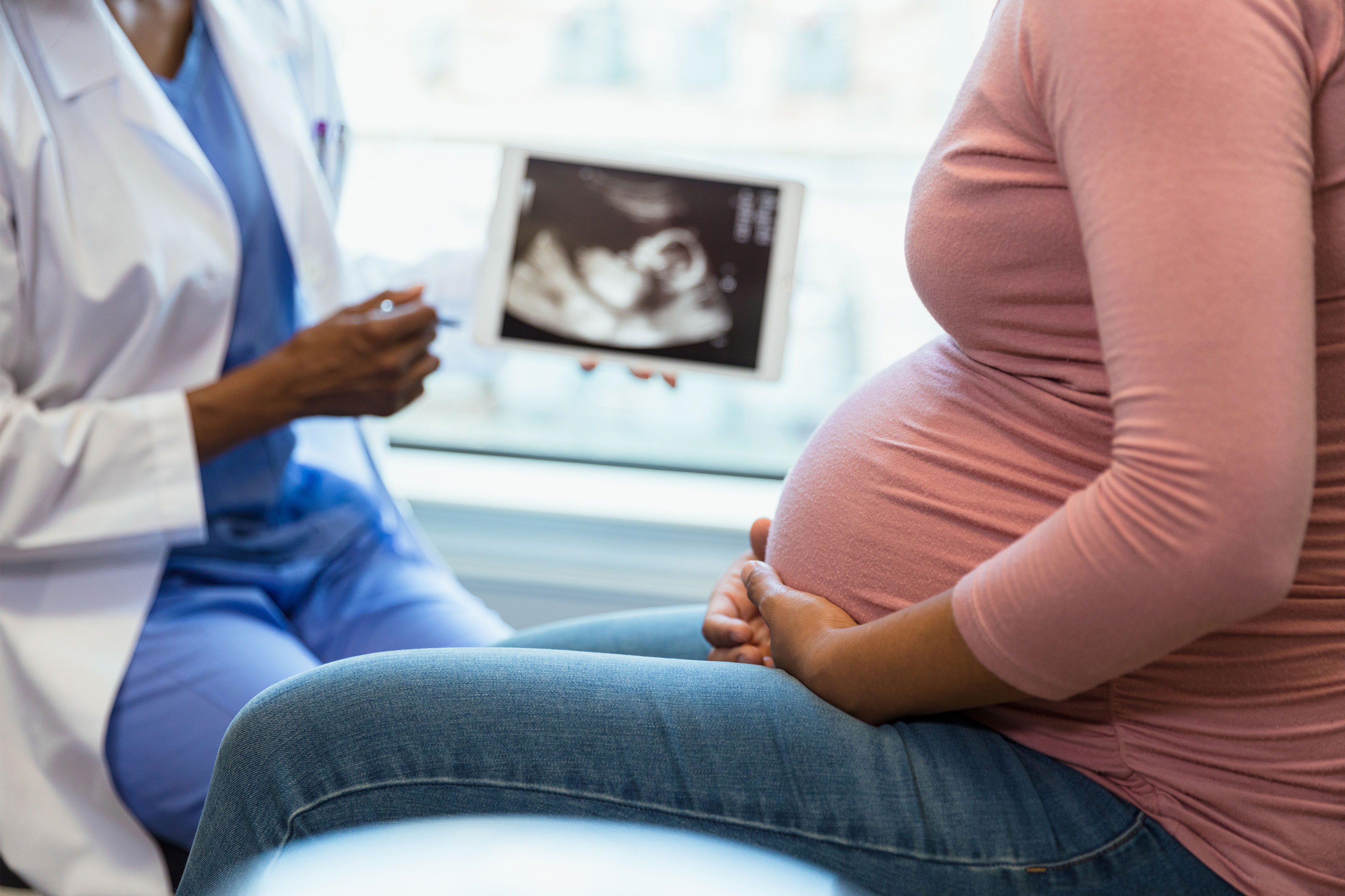 A photo of a black doctor showing a black pregnant woman an image of her ultrasound.