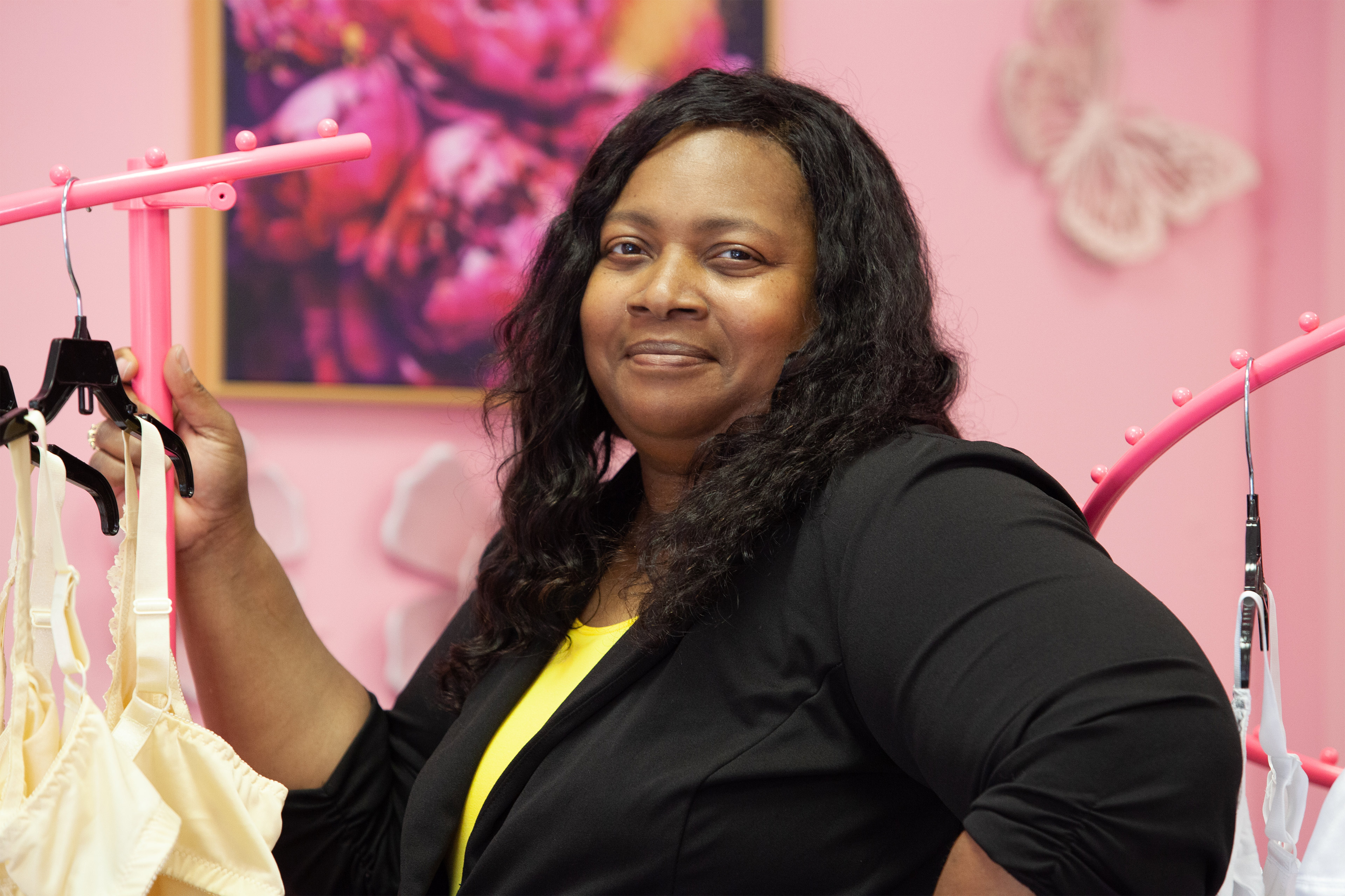 A photo of a Black woman posing for a photo by racks of clothing indoors.