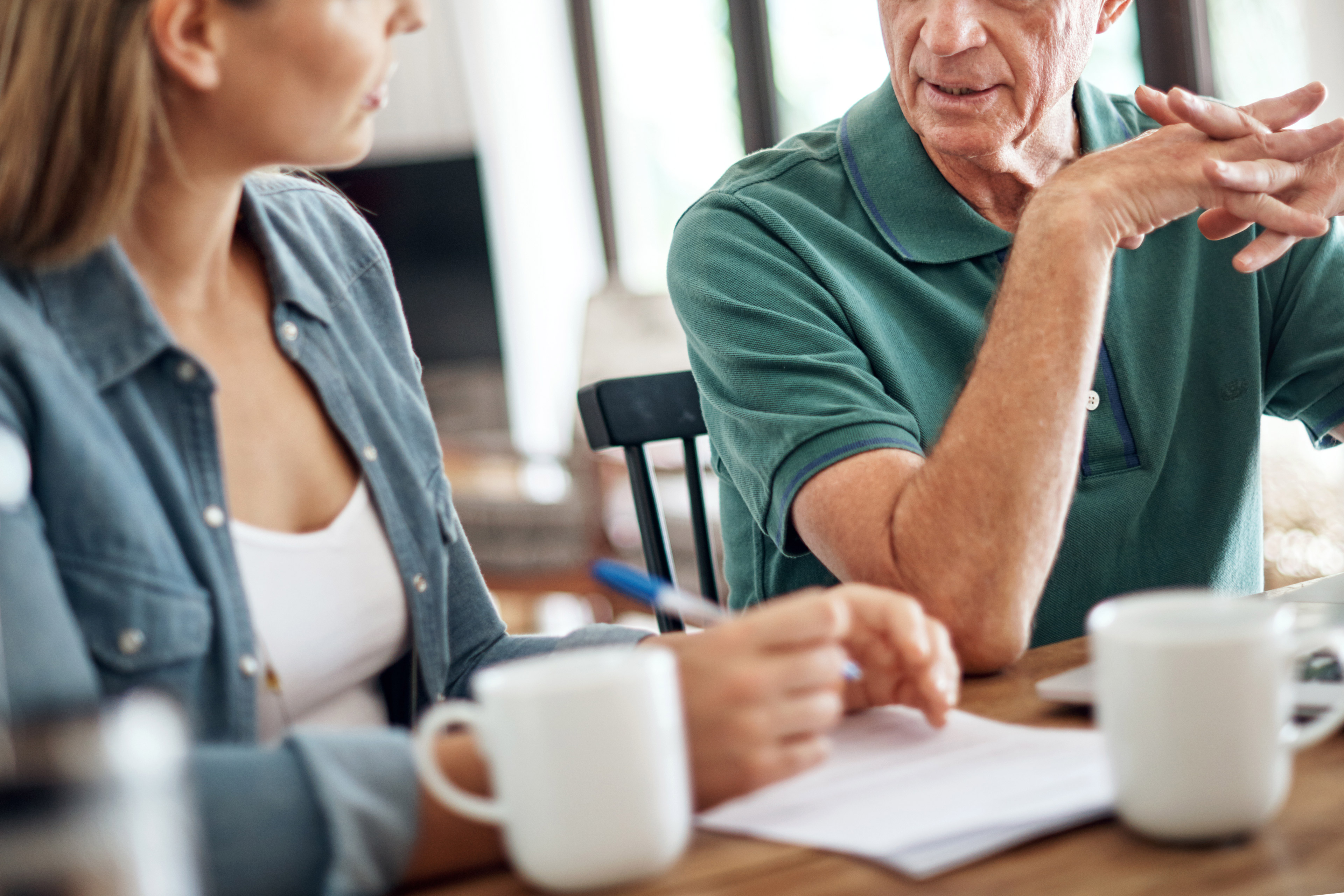 A photo of an adult daughter having a discussion and taking notes while talking to her aging father.