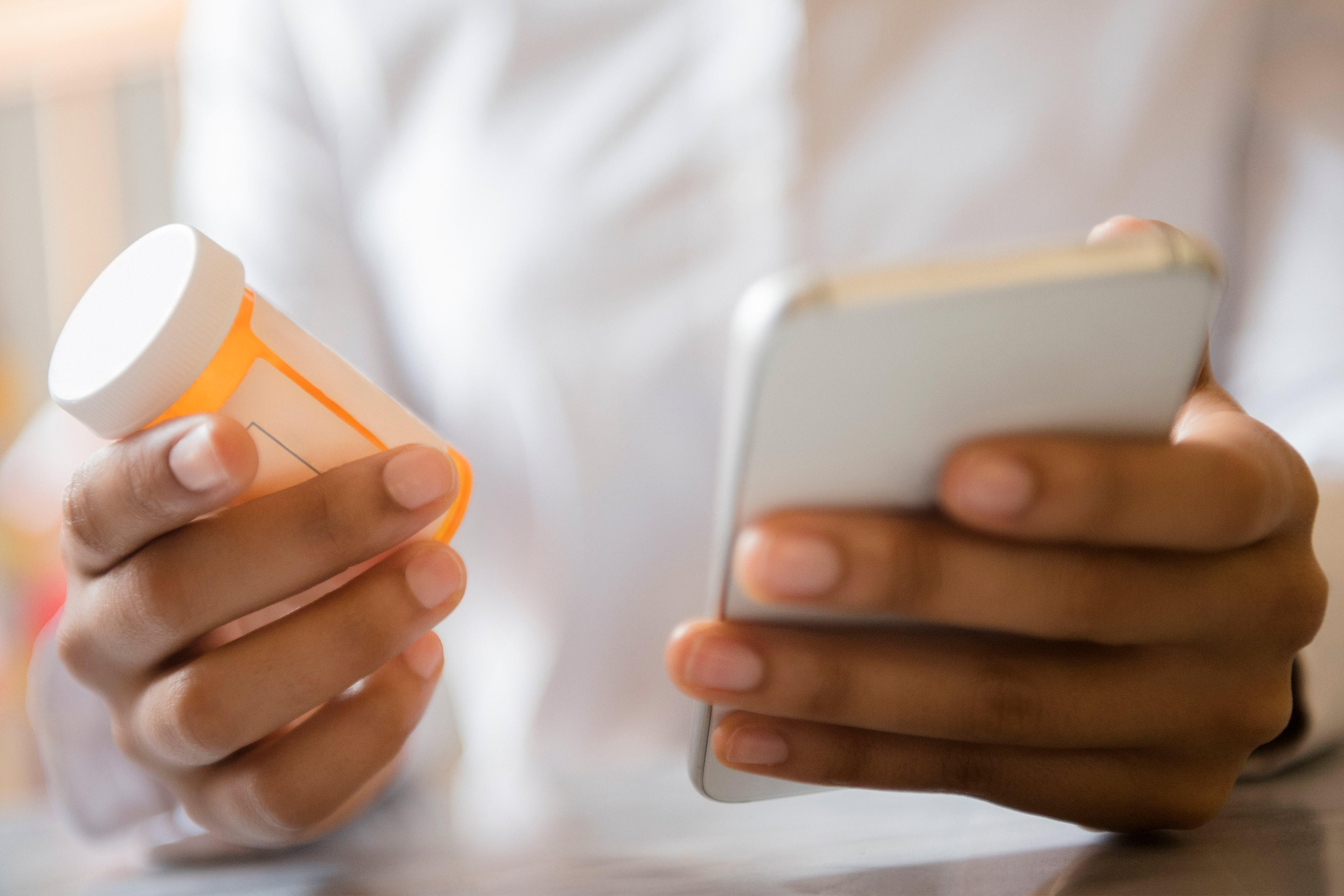 A photo of a woman's hands holding a pill bottle in one hand and a cell phone in the other.