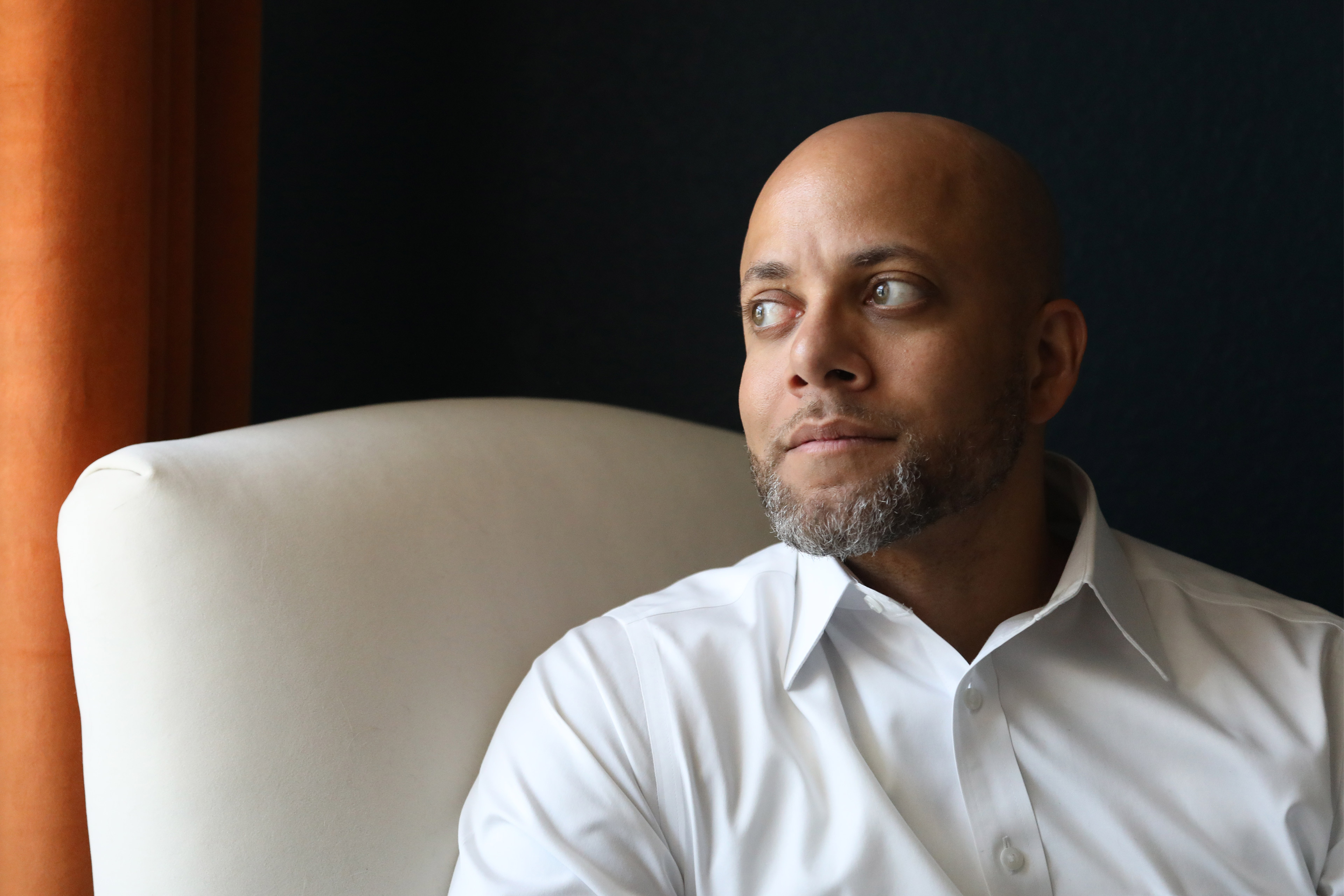 A portrait of a man sitting indoors and looking out a window.
