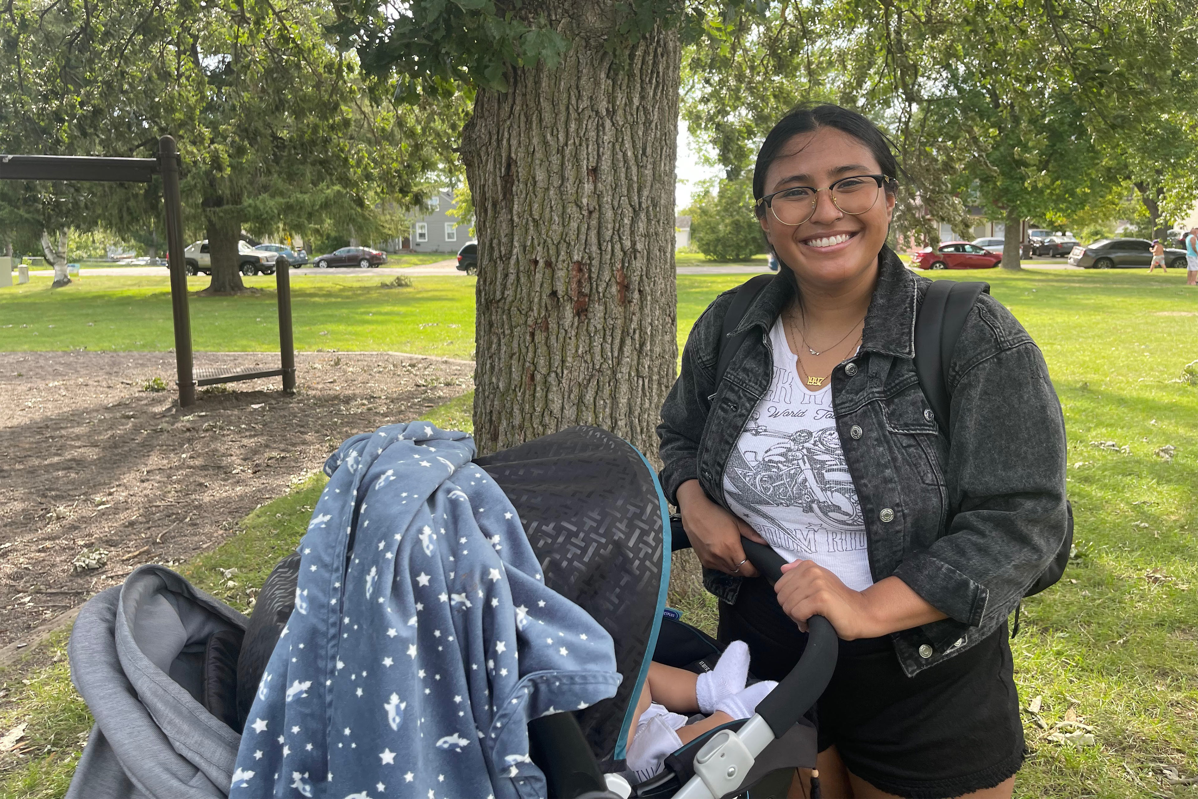 A photo of a woman standing outside next to a stroller.