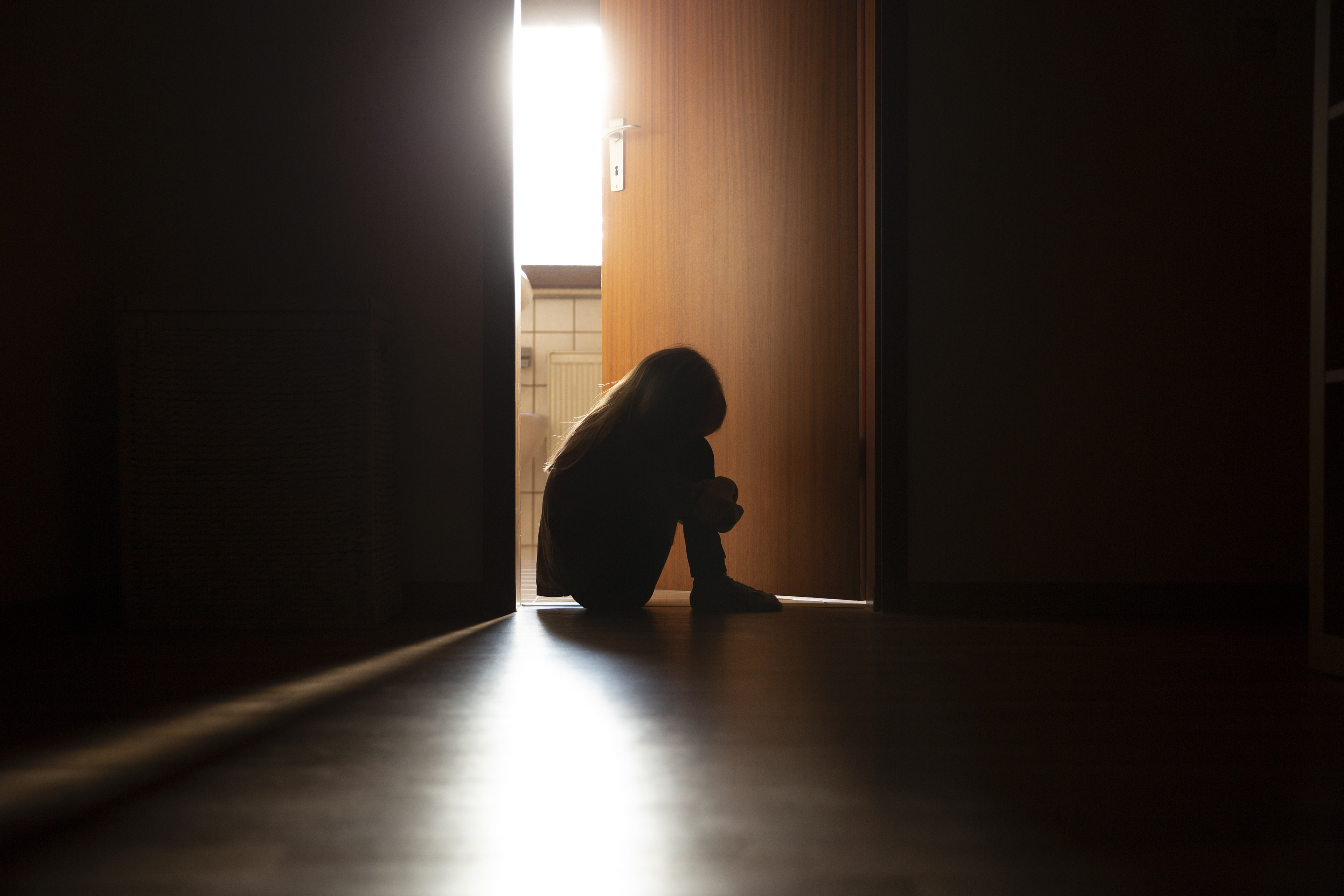 A silhouette of a child sitting in the doorway of a bathroom.