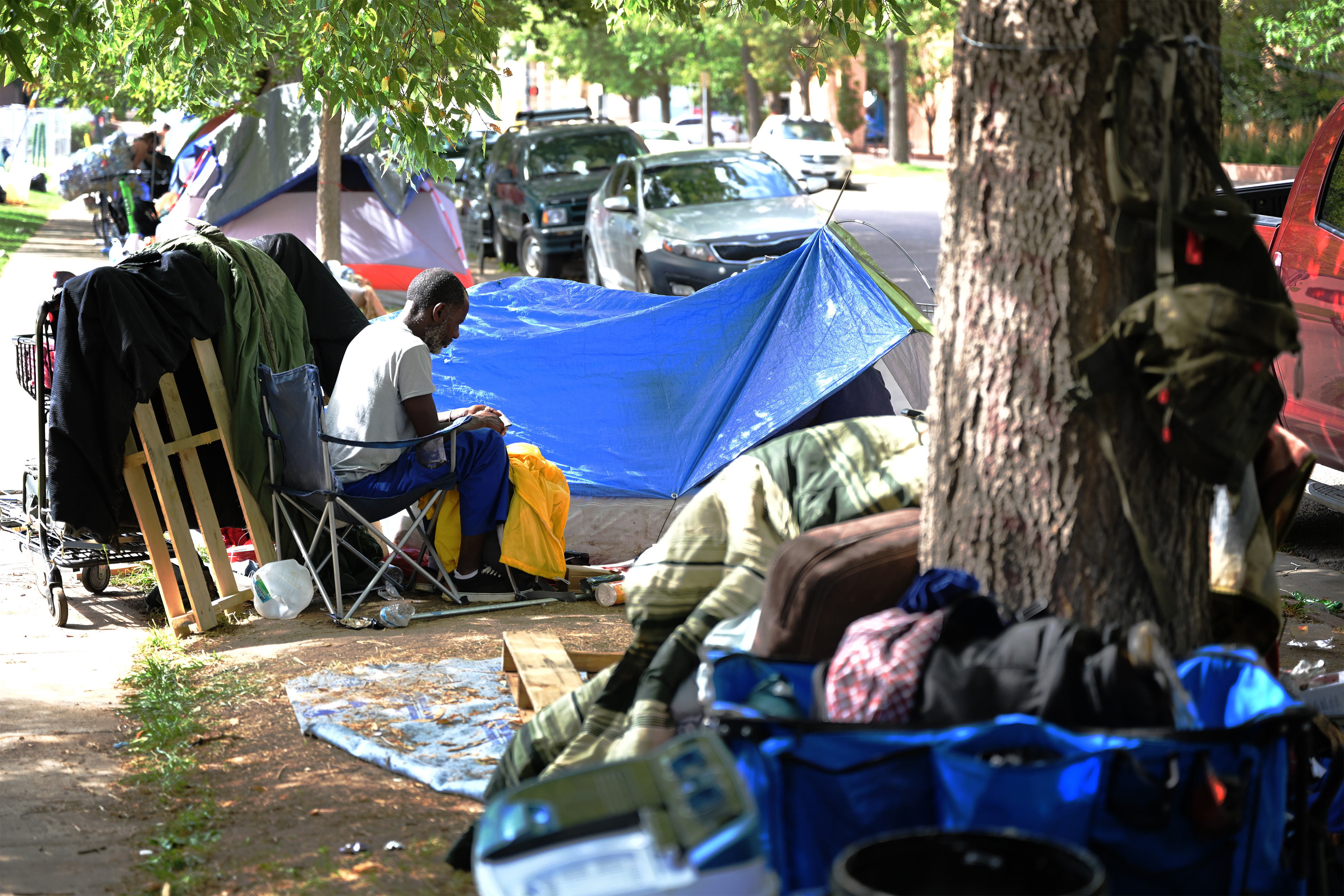 A photo of a man sitting by a tent in a homeless encampment.