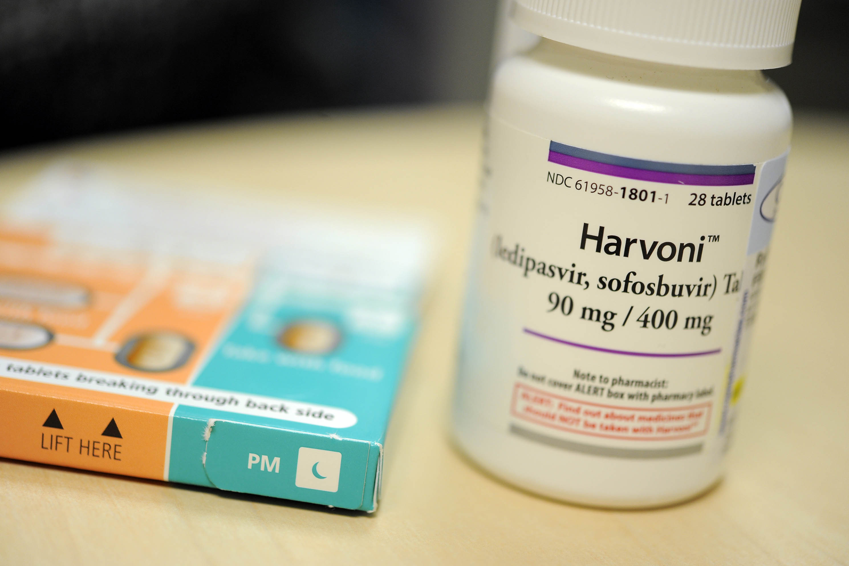 A photograph shows a white pill bottle of Harvoni, a drug to treat hepititis C.