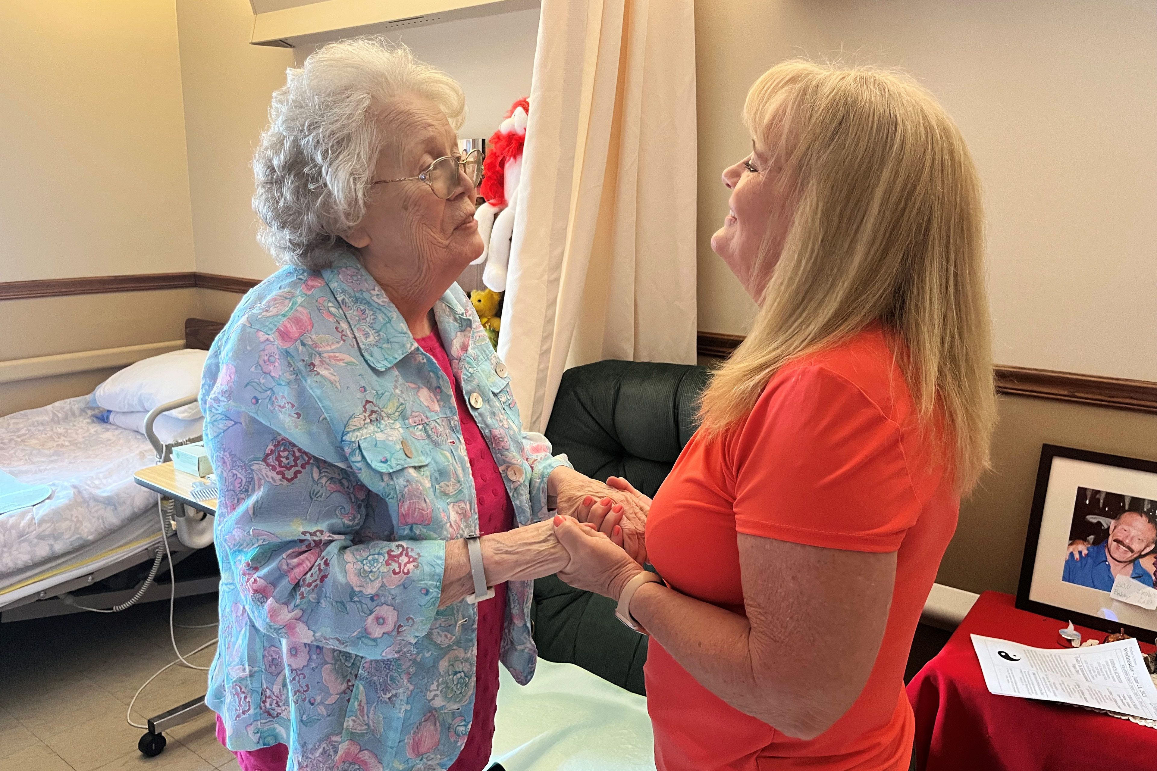 A photo of an older woman and a younger woman greeting one another and holding hands.
