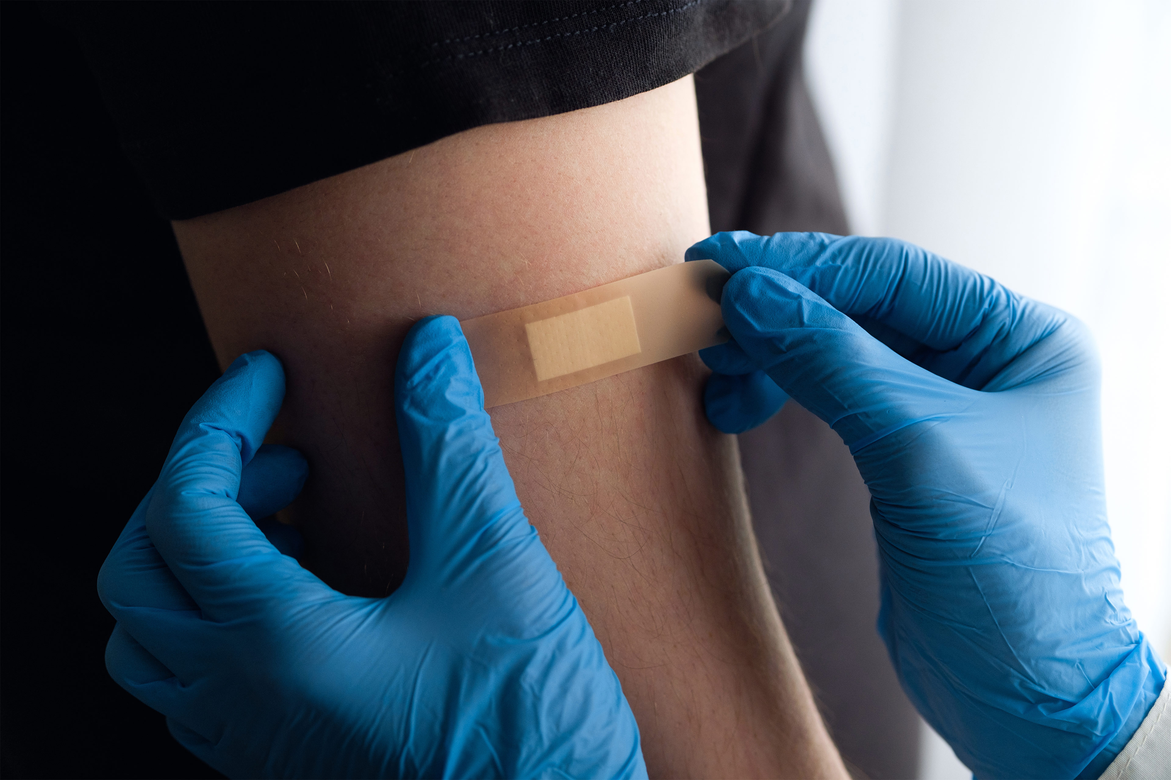 A photo of a medical worker's gloved hands applying a bandage to a patient's arm after a vaccine.