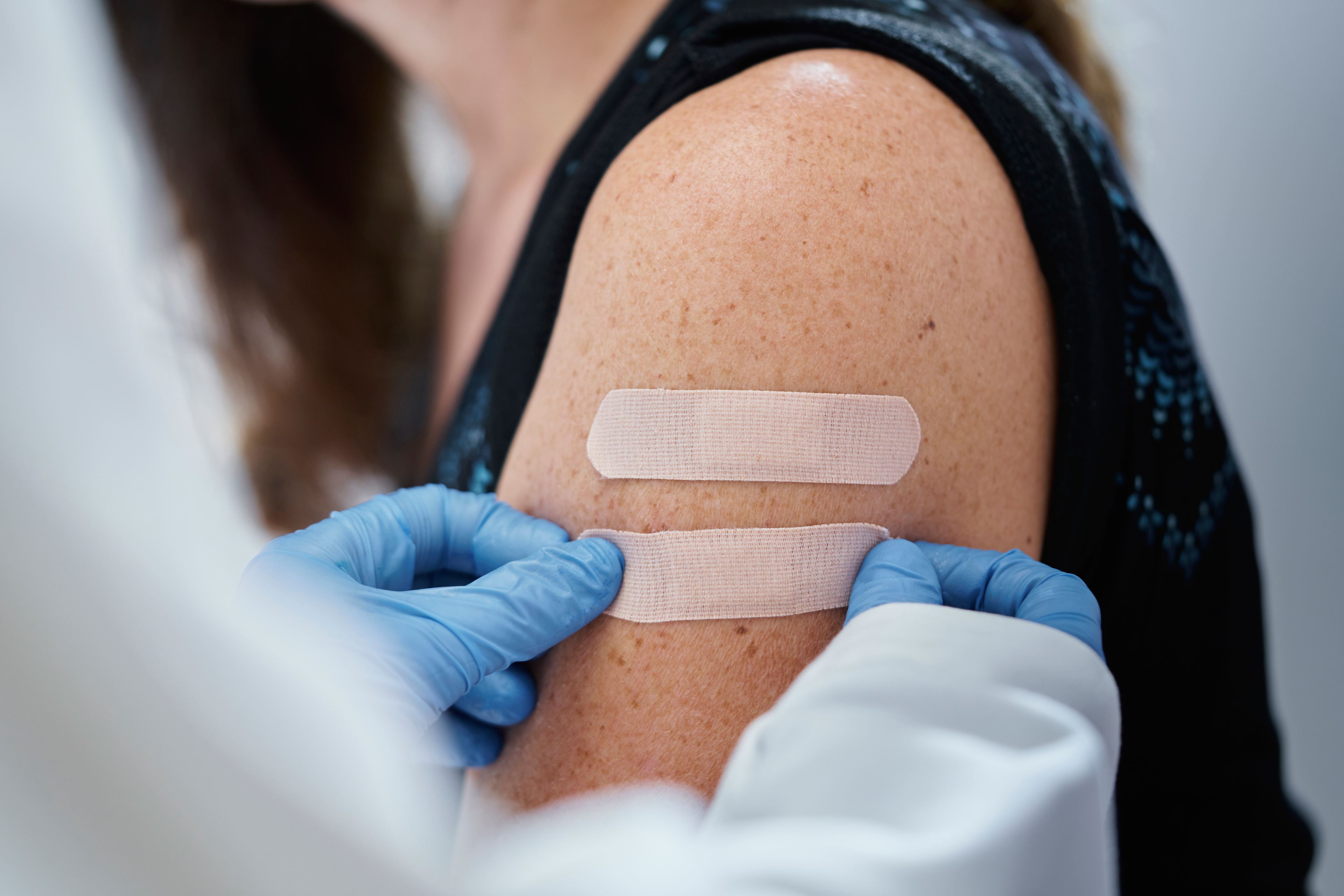A photo of a woman's arm as a medical worker puts a second bandage after giving the woman vaccines.