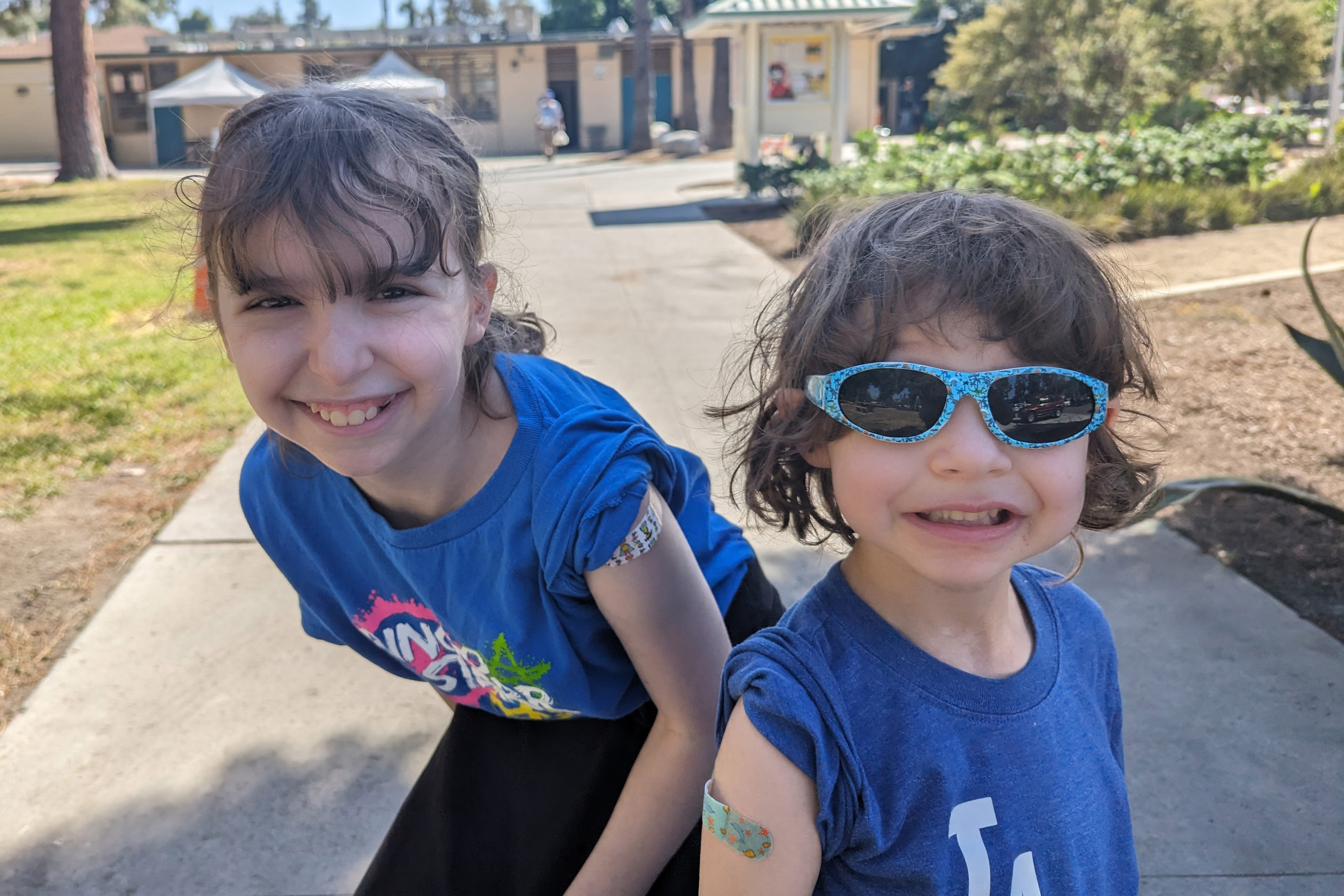 A photo of two children smiling for the camera showcasing bandages on their arms after getting vaccinated.