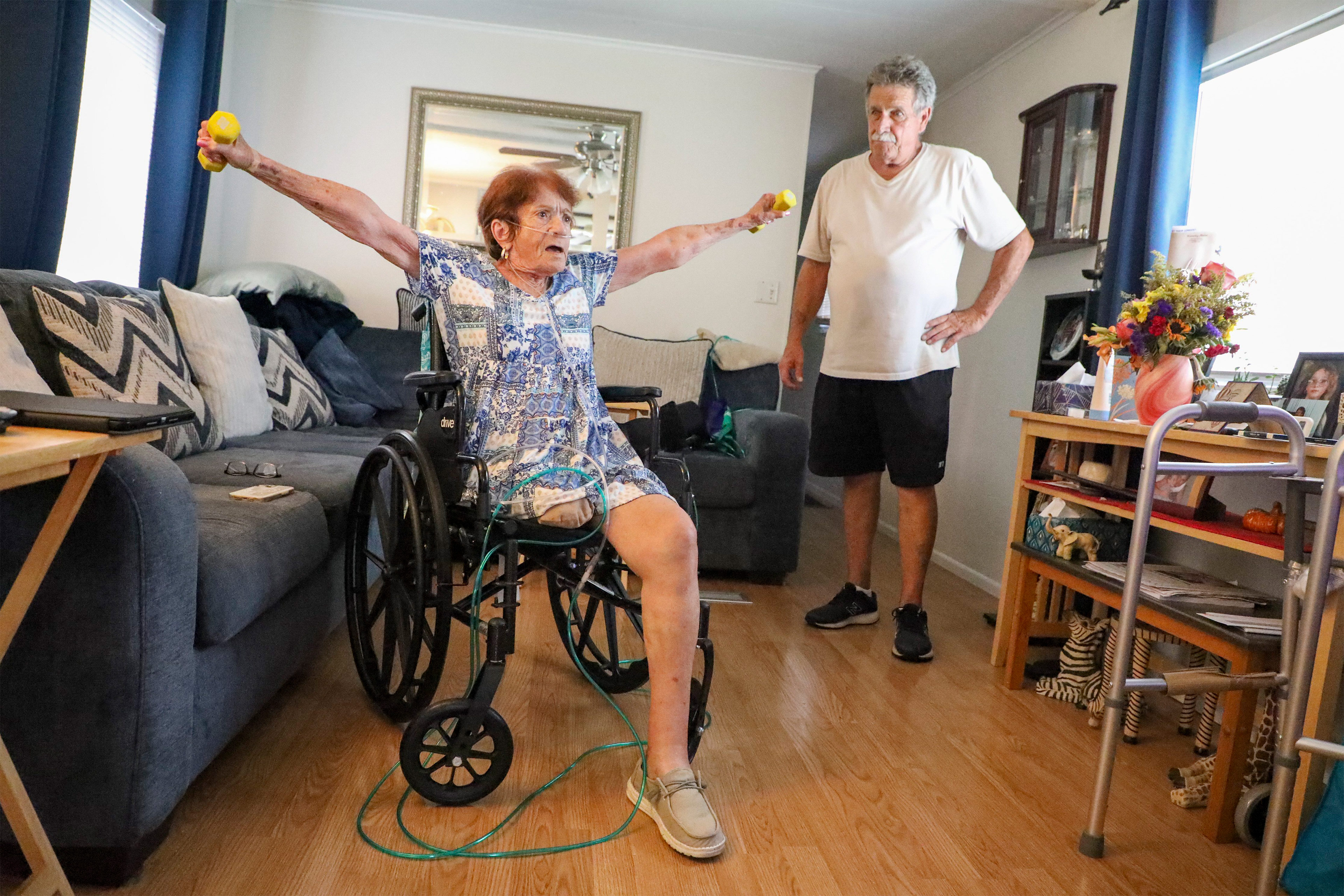 A photo of a woman in a wheelchair lifting hand weights. Her right leg is amputated.