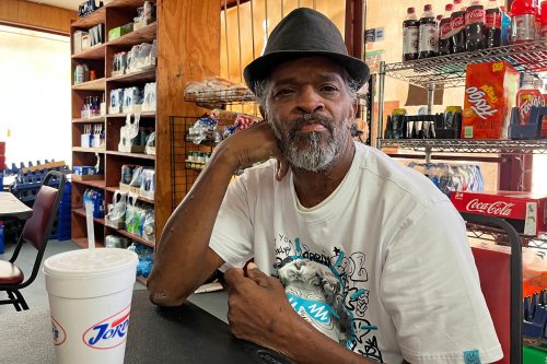 A photo of a man sitting indoors, wearing a hat, and looking at the camera.
