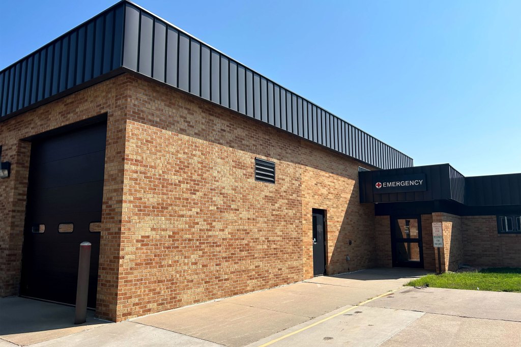 The exterior of a building. A sign above the door reads "Emergency".