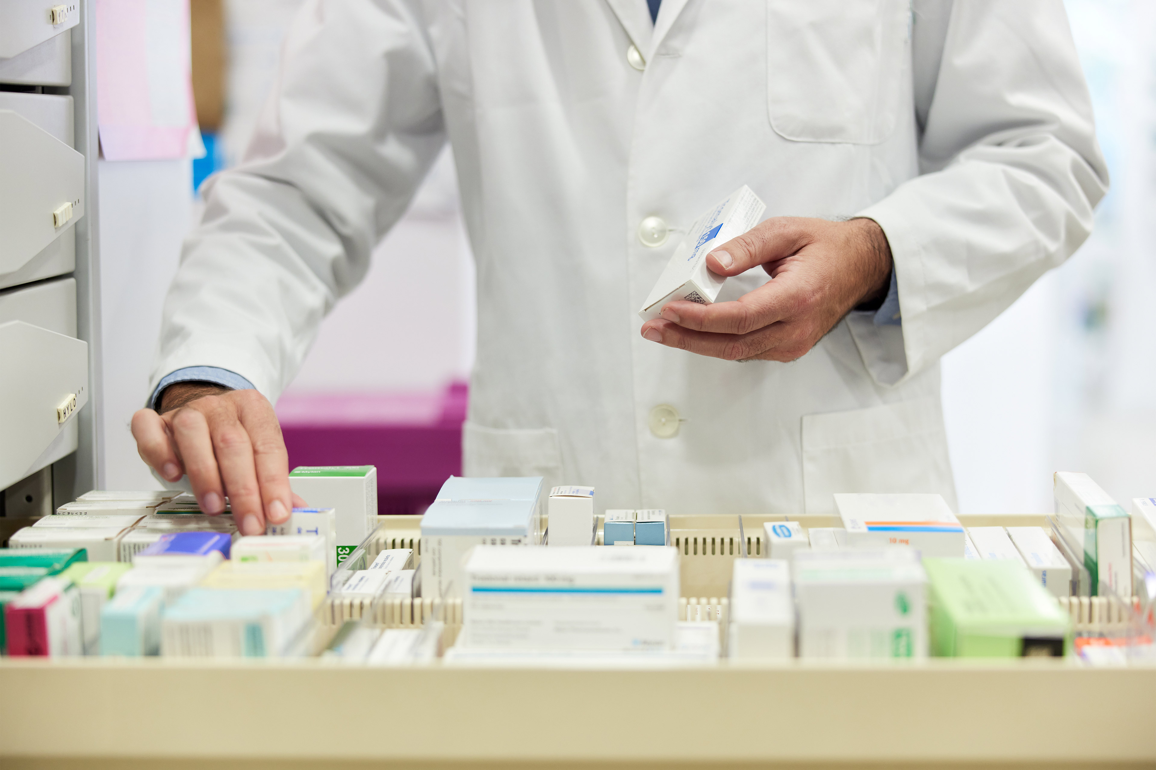 A photo of a pharmacist organizing boxes of pills in an opened drawer.