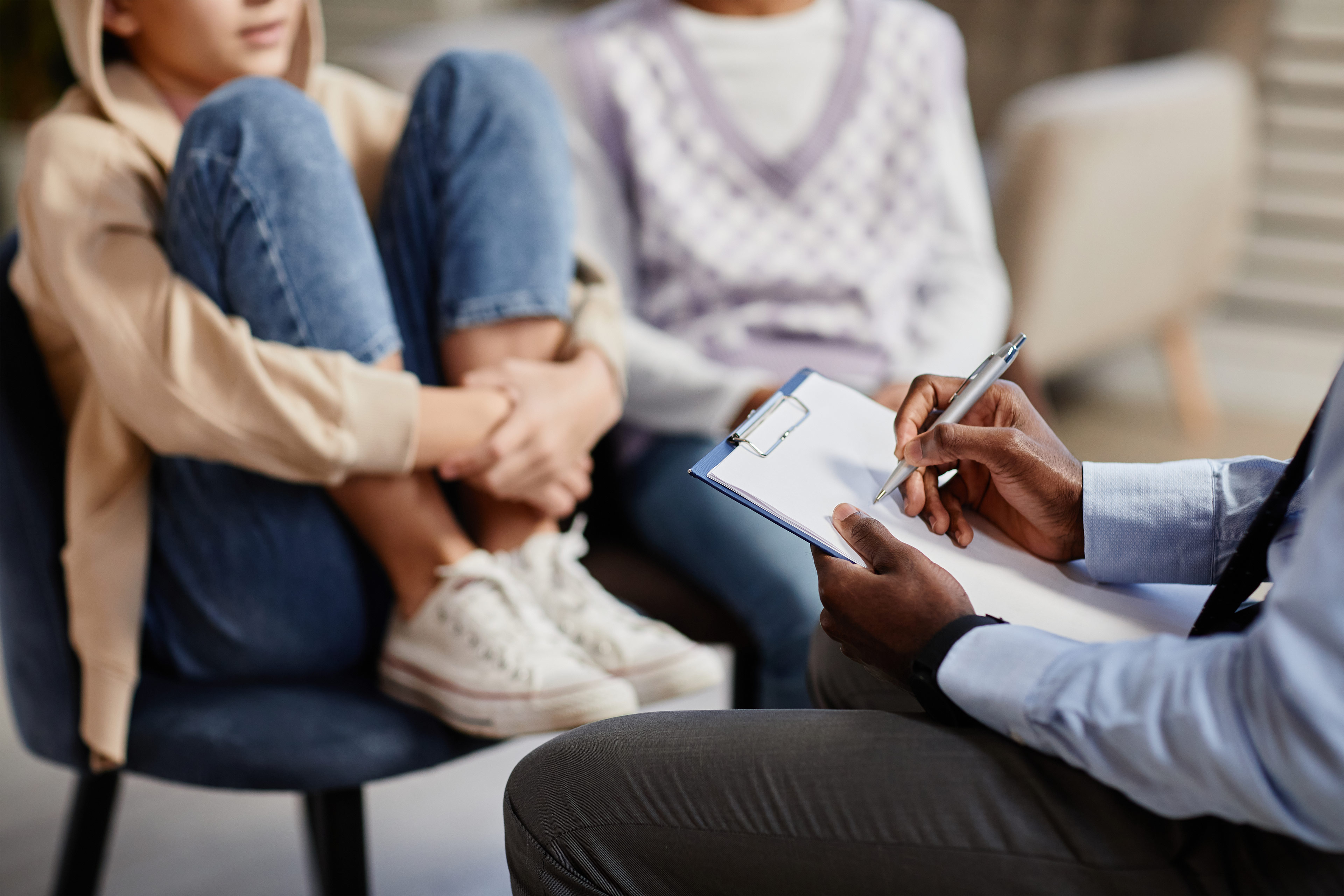 A photo of an adolescent sitting in a chair with their parent while a medical professional takes notes on a clipboard.