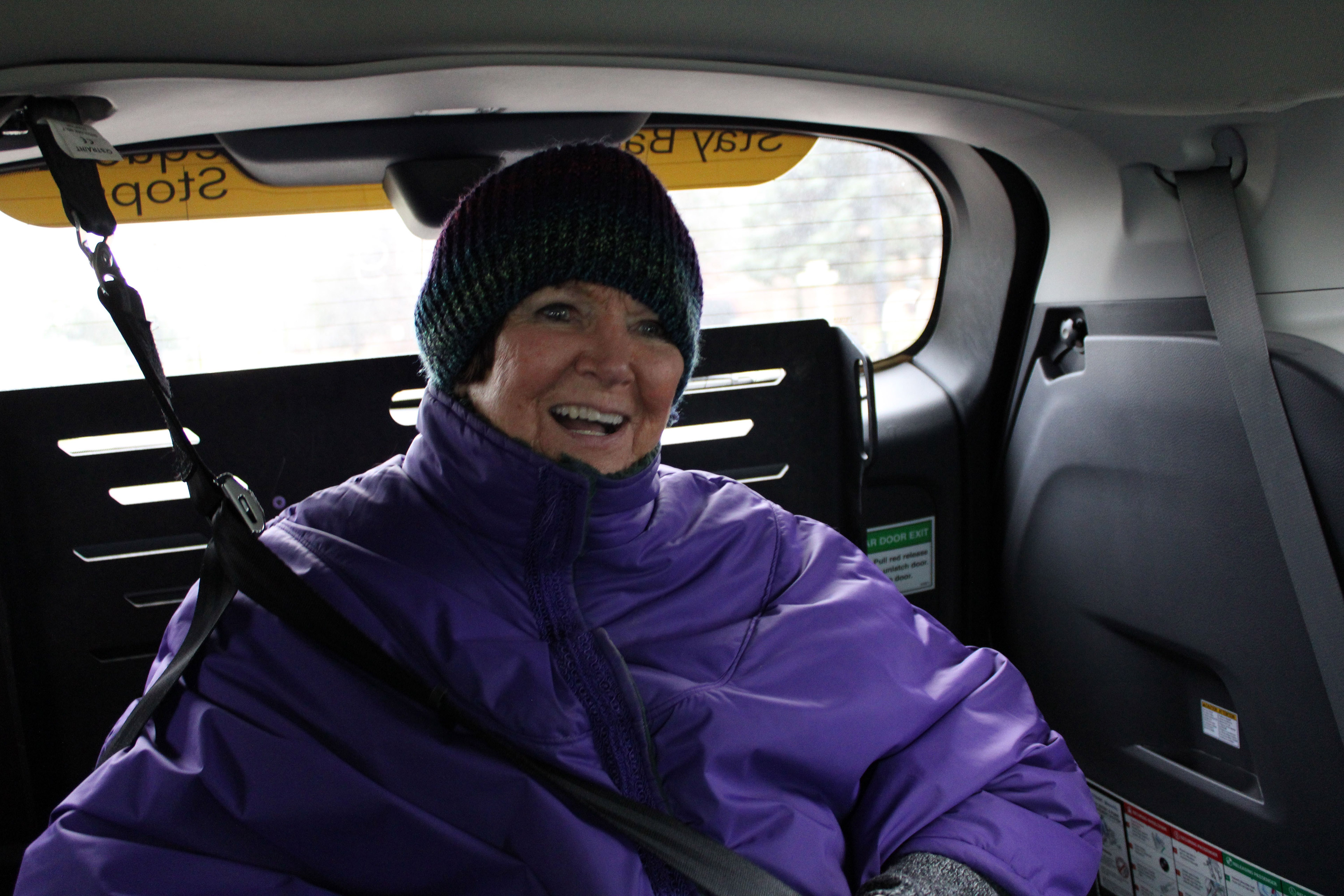 A portrait of Myrna Peterson. She is sitting in an electric wheelchair which is secured in the back of the goMARTI van.