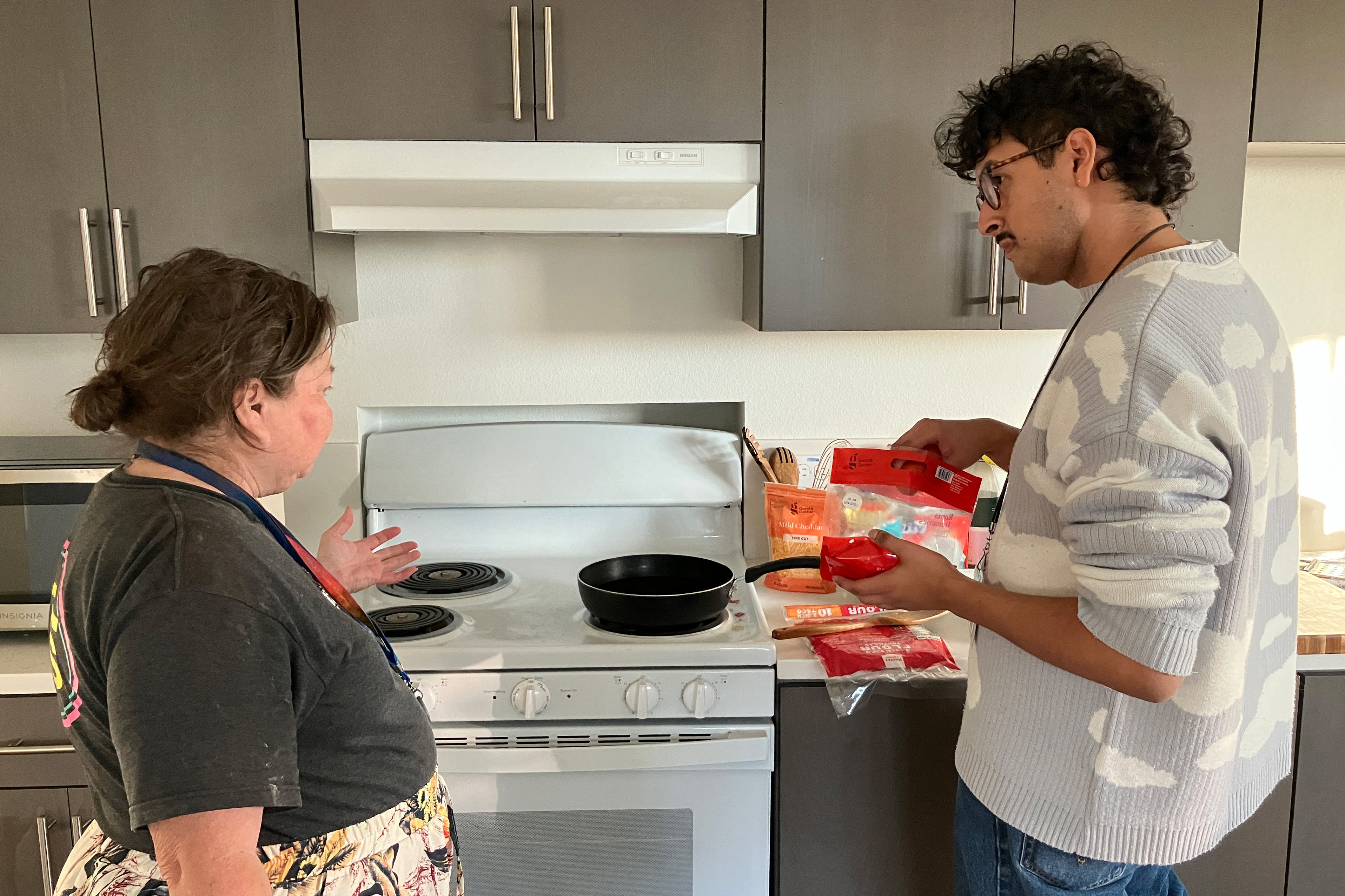 Carla Brown and Julian Prado stand beside a stove in Brown's home. They prepare to make hard-shell tacos.