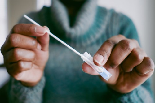 A photo of a woman's hands dipping a nasal swab into a small vial of solution as part of a covid-19 test.