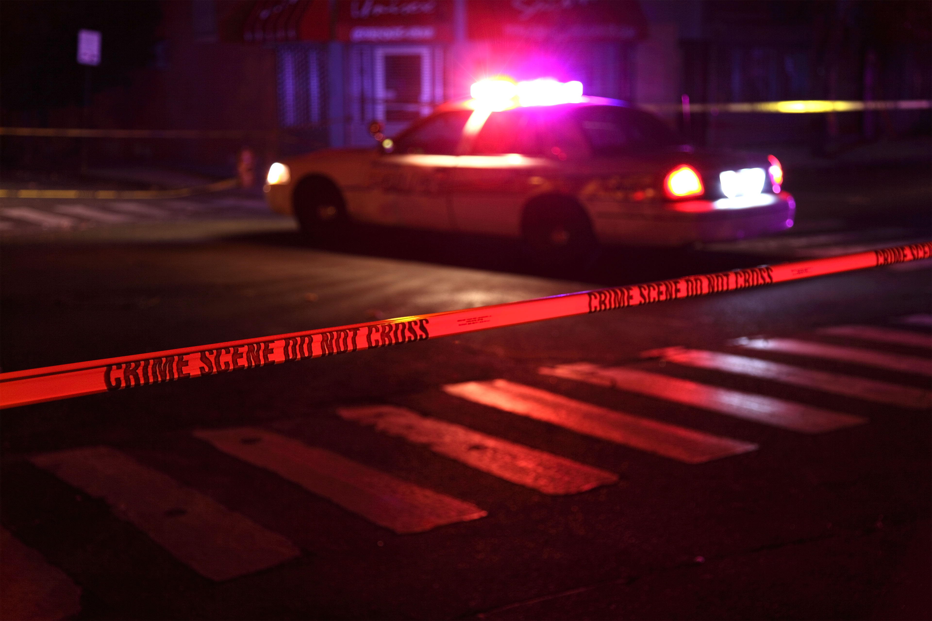 A photo of a police squad car with flashing lights on and crime scene tape in the foreground.