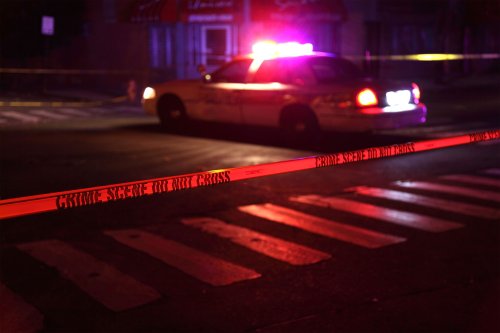 A photo of a police squad car with flashing lights on and crime scene tape in the foreground.