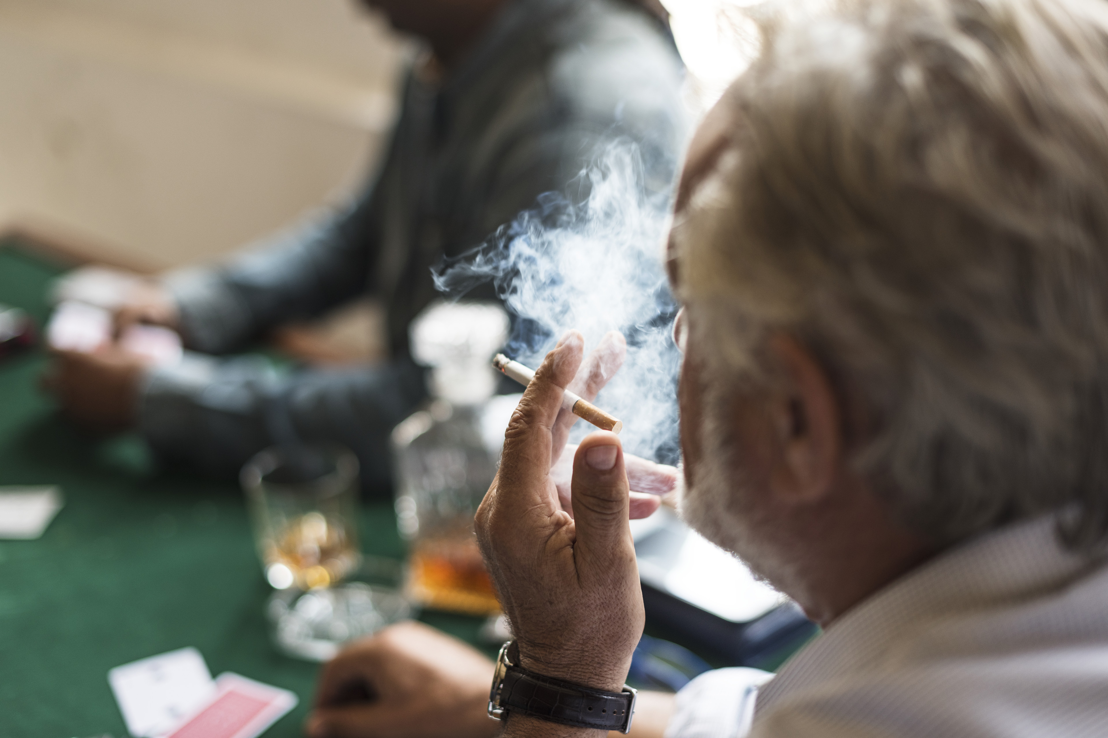 A side view of man smoking cigarette while playing a card game.