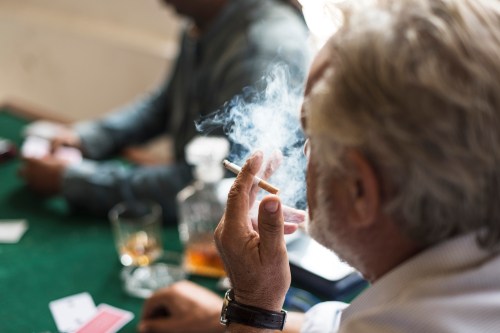 A side view of man smoking cigarette while playing a card game.
