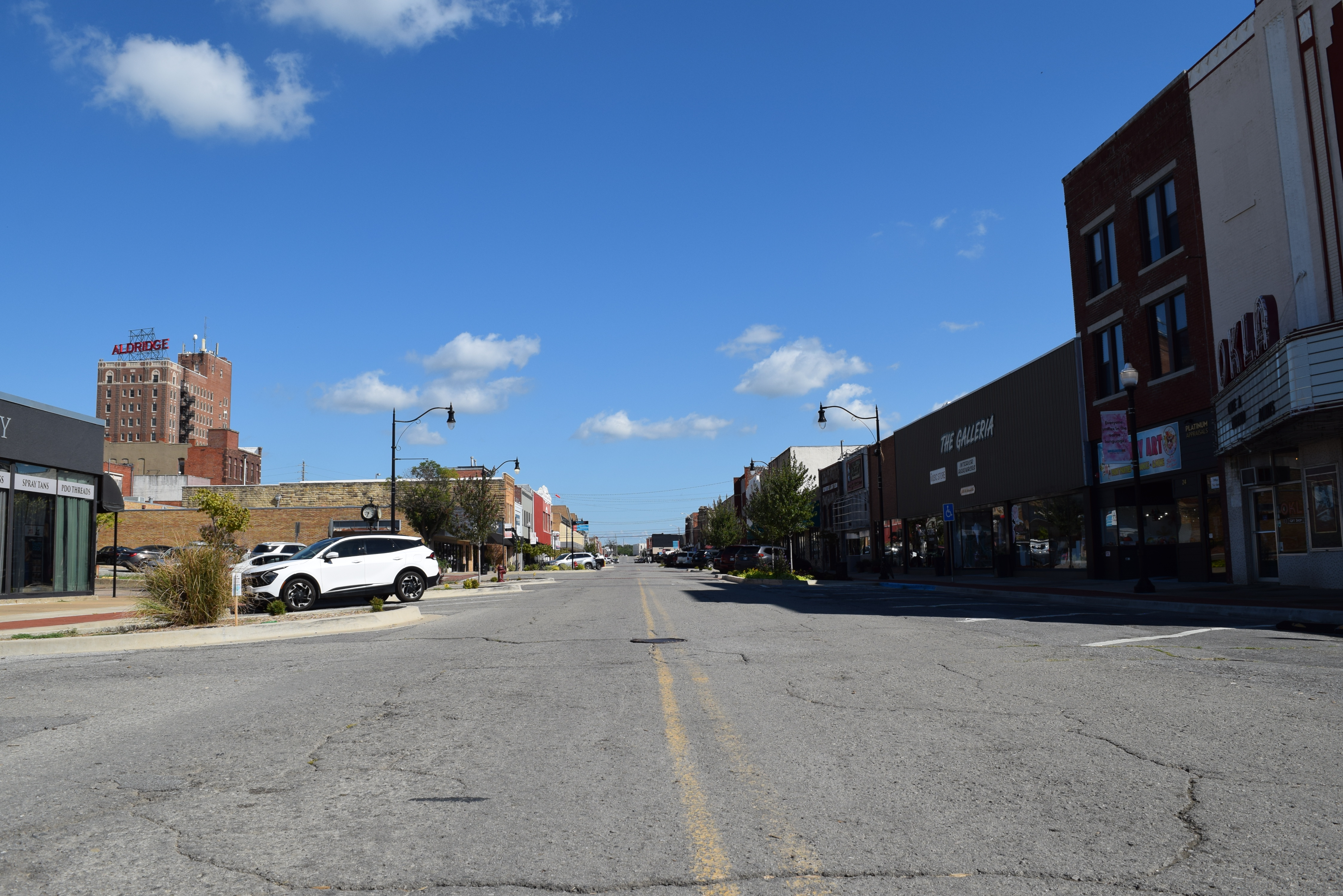 A wide shot a an empty road with one white car parked and several buildings along the street