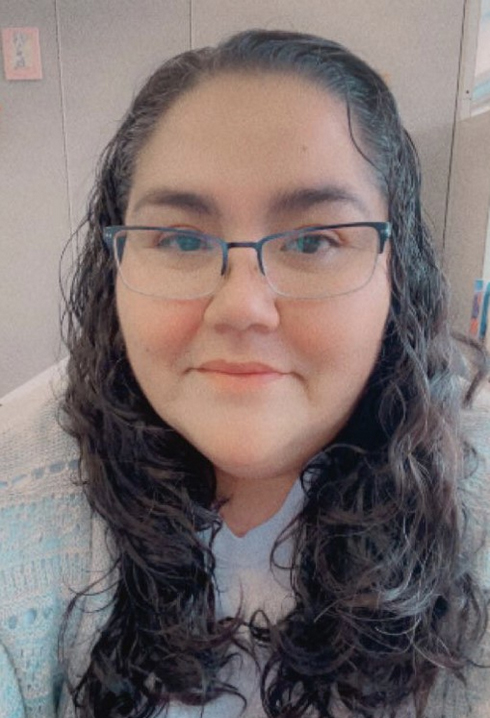 A portrait of Amanda Morningstar. She has long, wavy brown hair and wears glasses.