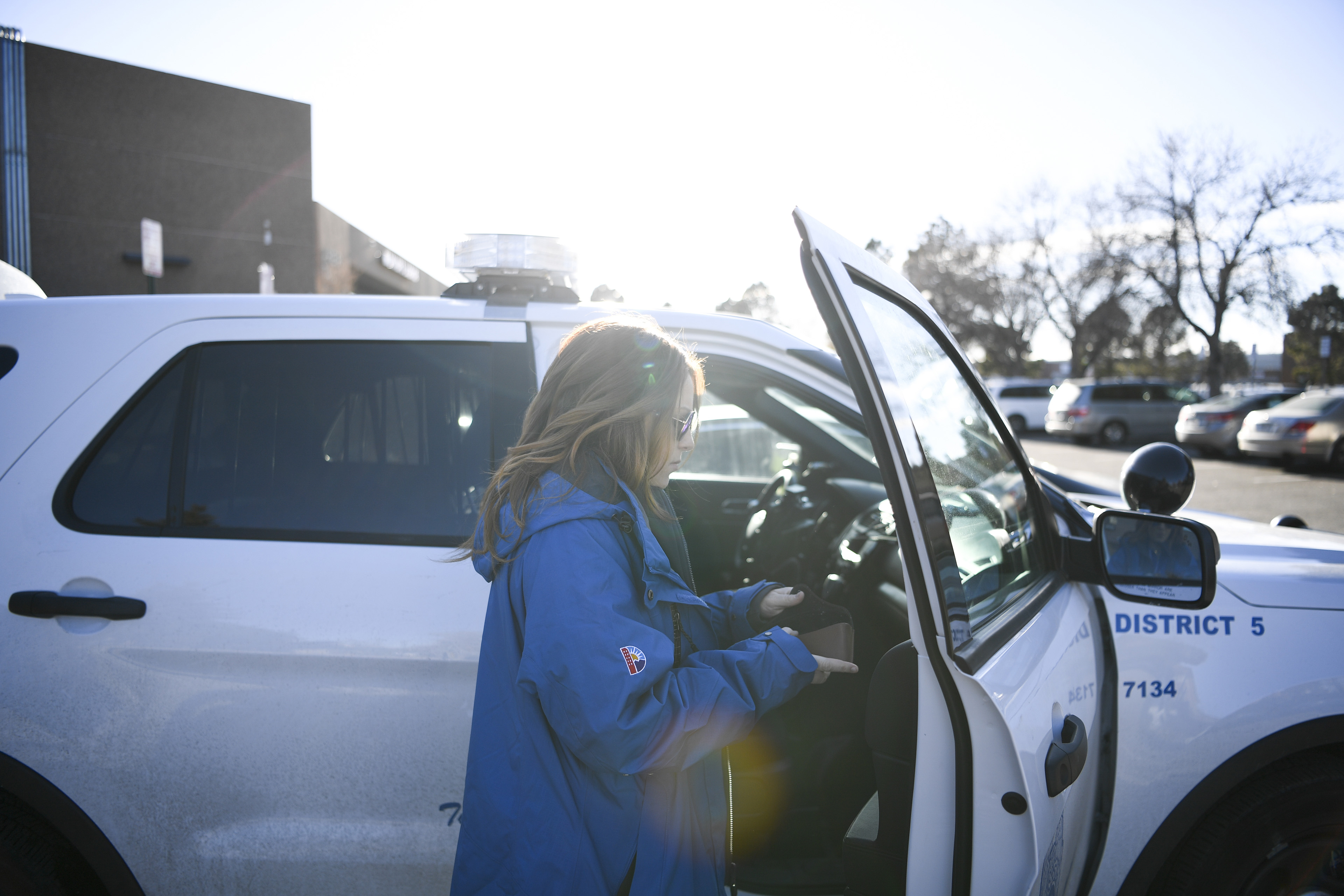 A woman wearing sunglasses and a blue jacket gets into a white police sport utility vehicle