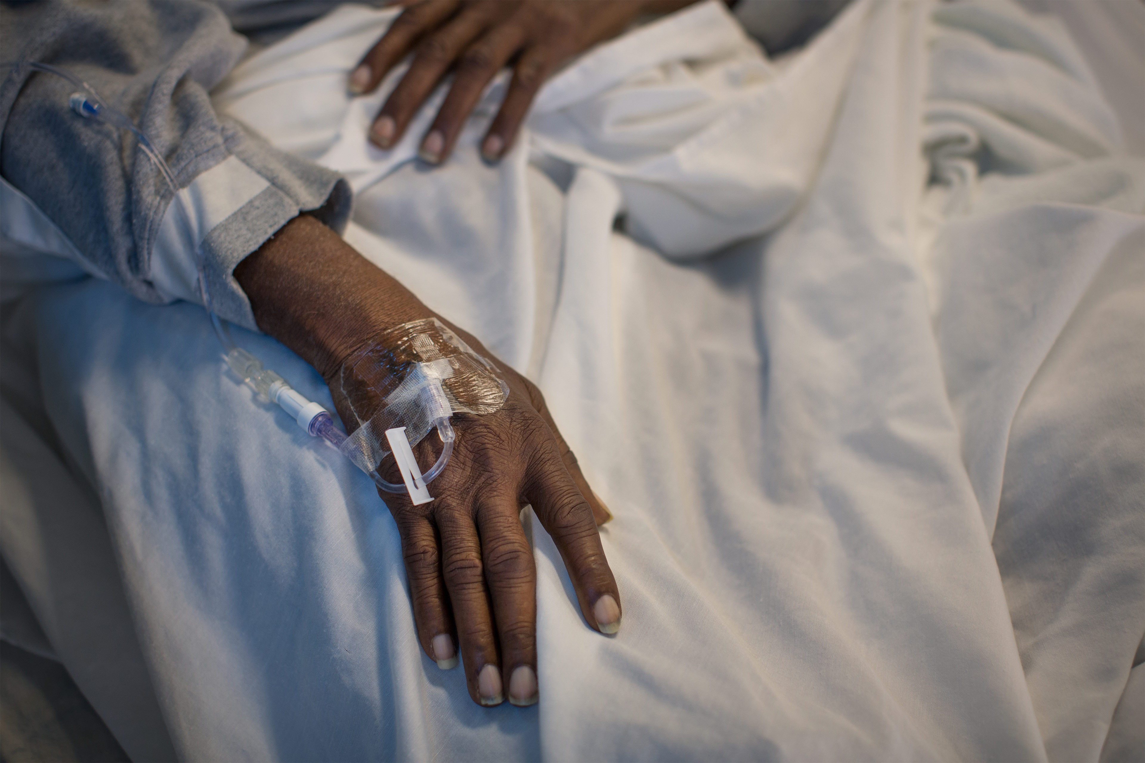 A photo of a black man's hand with an IV in the top of his hand.