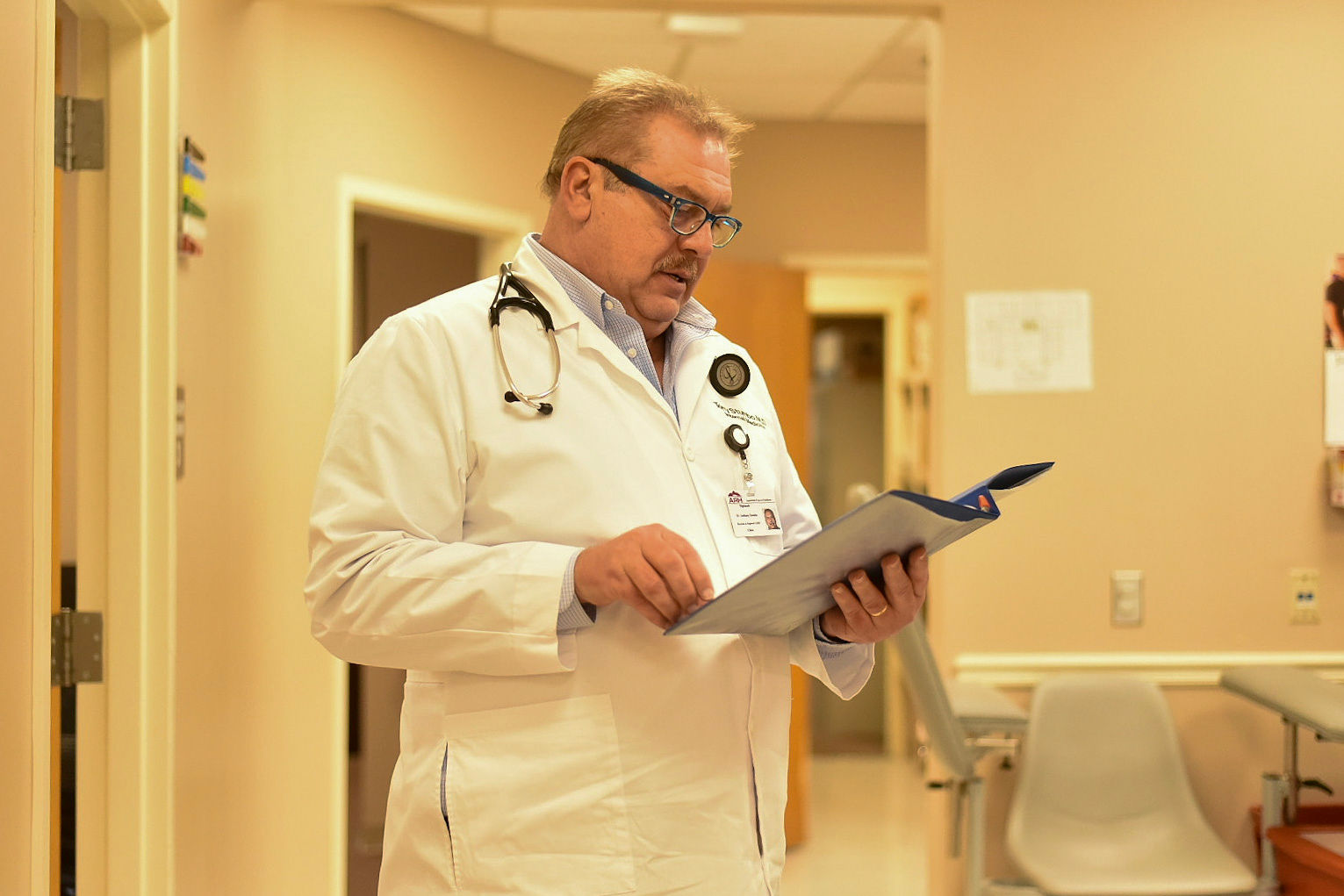 A photo of a doctor standing indoors and looking at a binder.