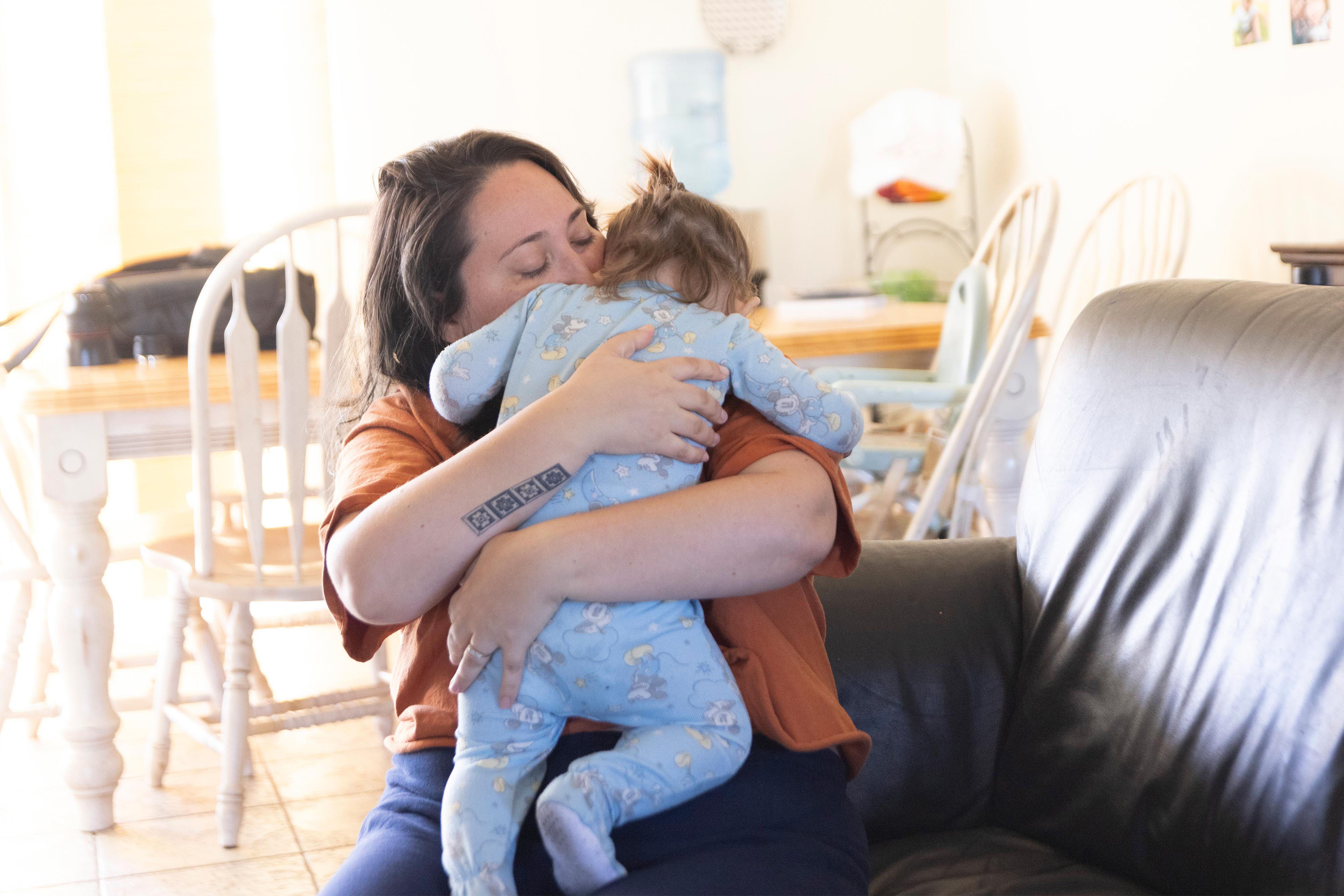 A photo of a mother hugging her infant son while sitting on the couch.