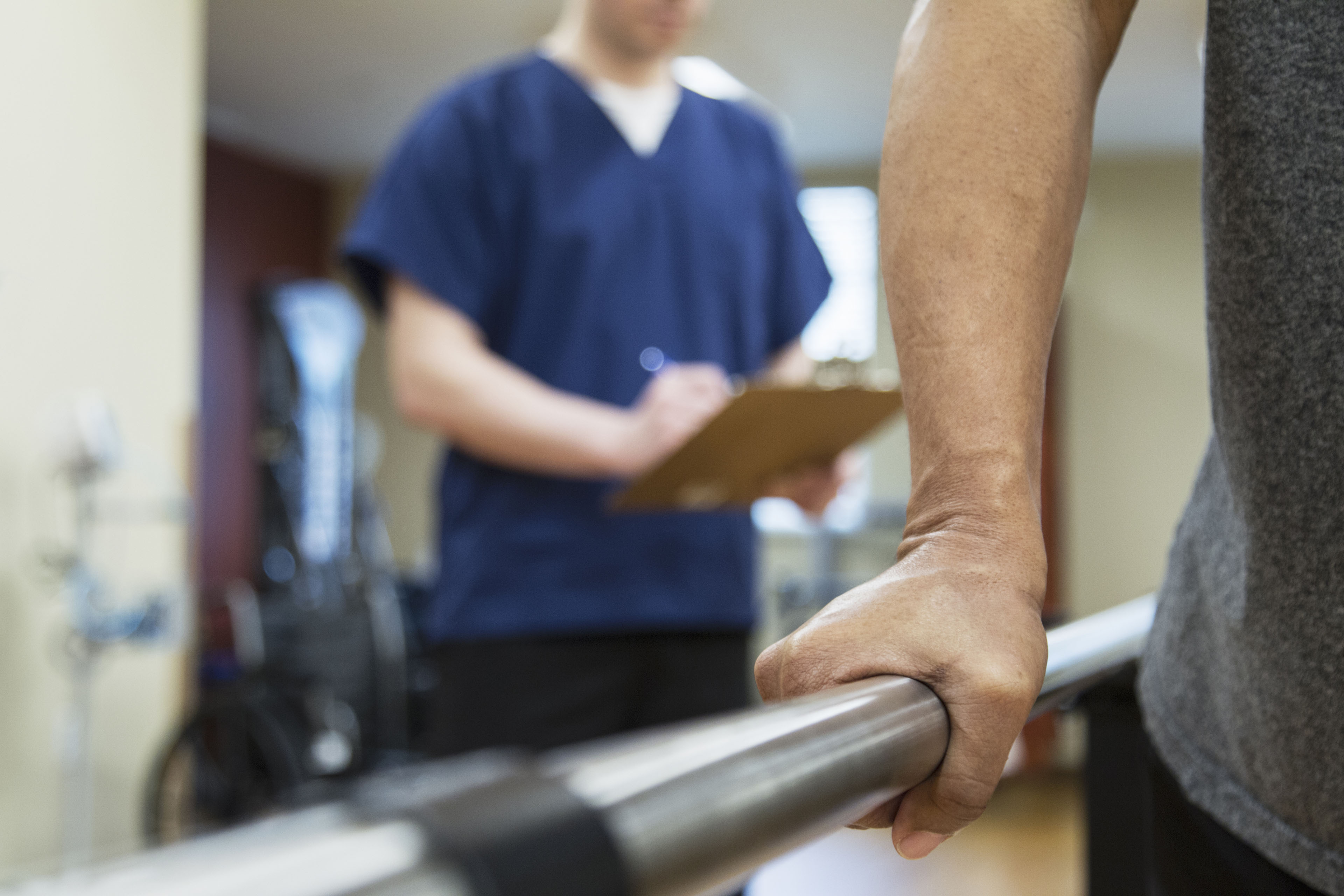 An unidentifiable patient is undergoing physical therapy while a health care professional takes notes behind them.