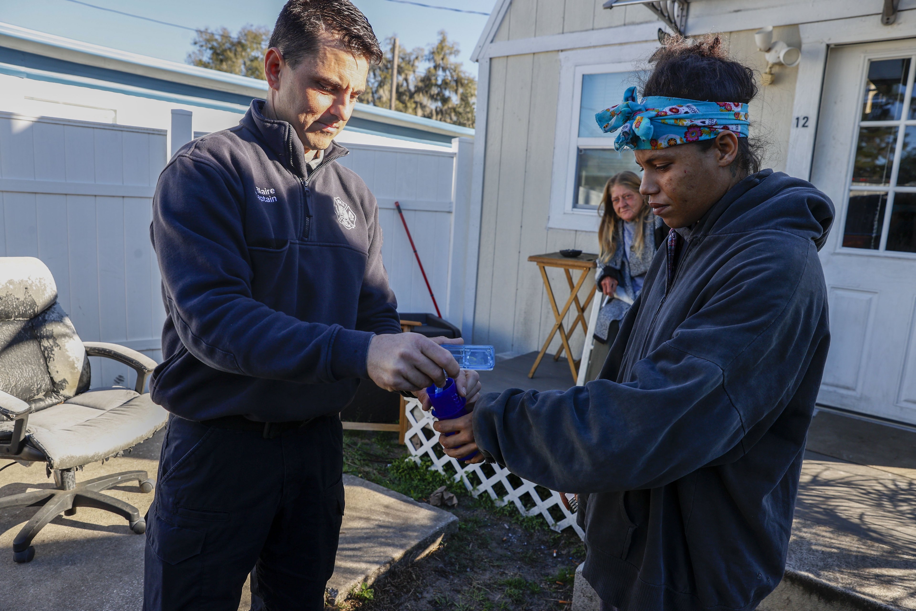 A male EMS hands a woman medication. In the background, a third woman looks on.