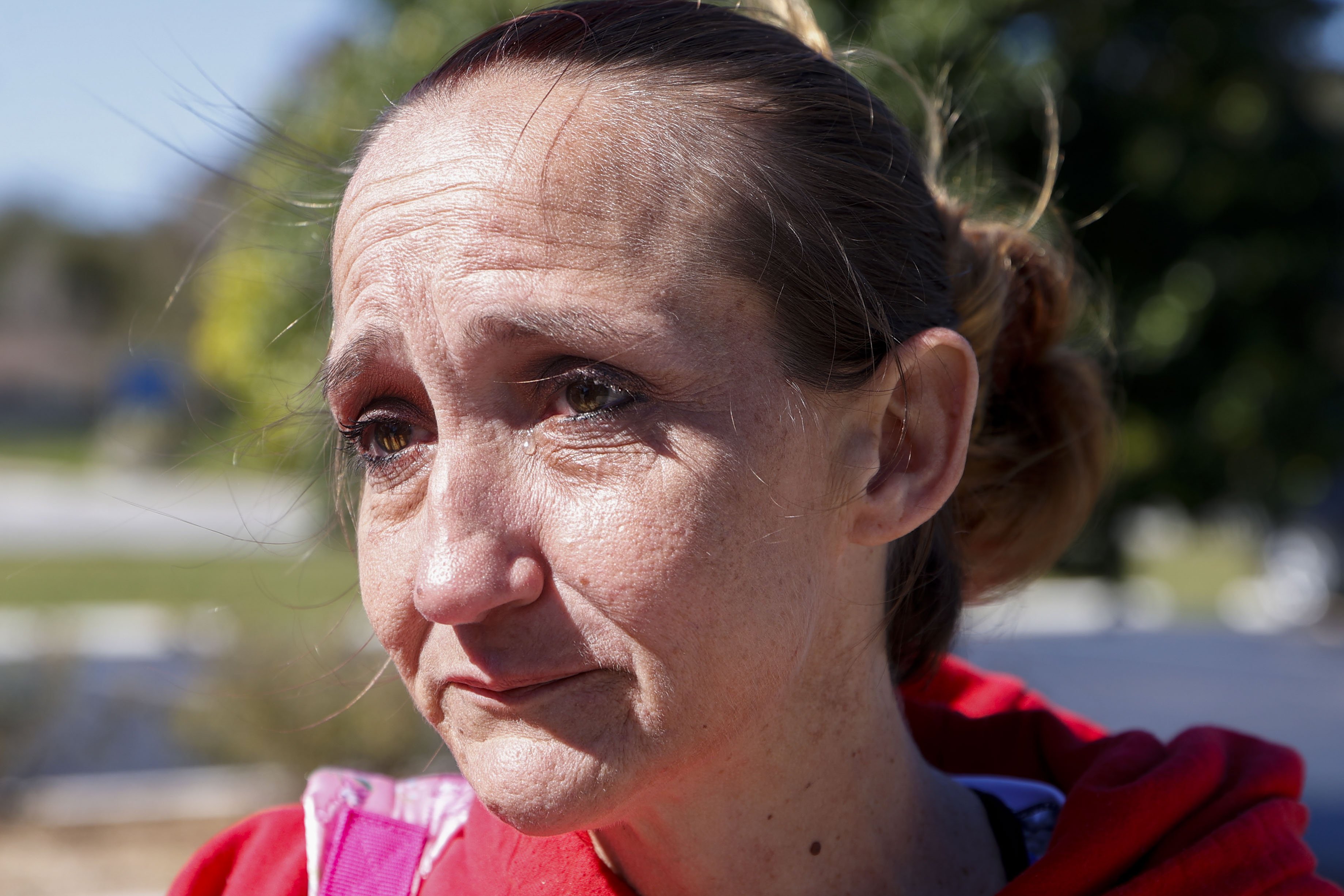 A close up of a woman's face. She is wearing a red  shirt and crying.