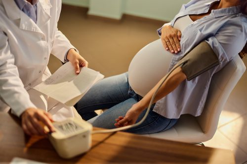 A photo of a pregnant woman having her blood pressure measured by a doctor.
