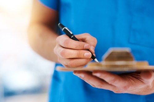 A cropped shot of a nurse writing on a clipboard.