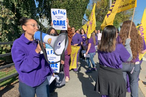 A photo of protesters standing outside. One holds a sign that reads, "Be fair to those who care."