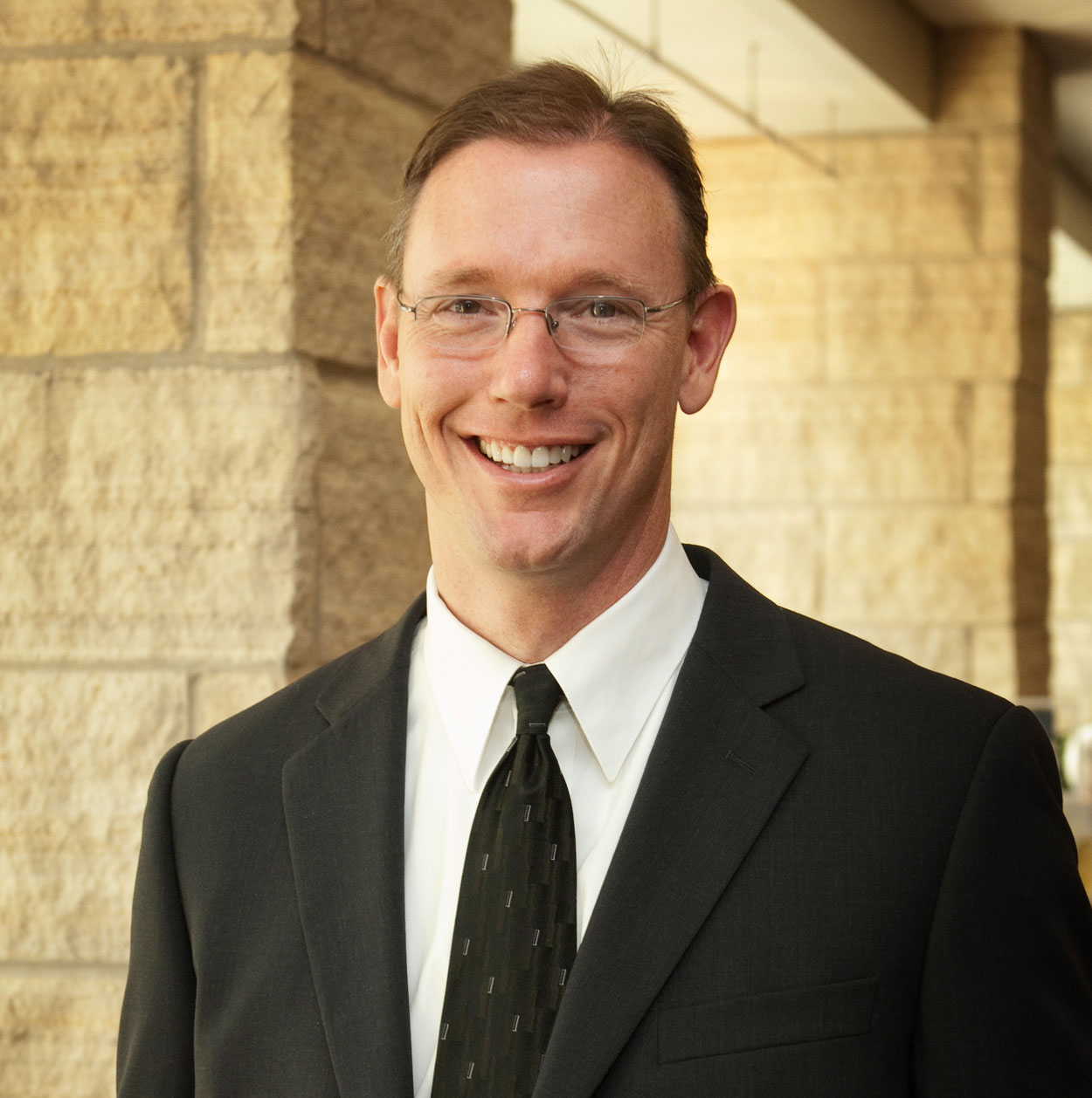A photo of a man in a suit smiling outside.