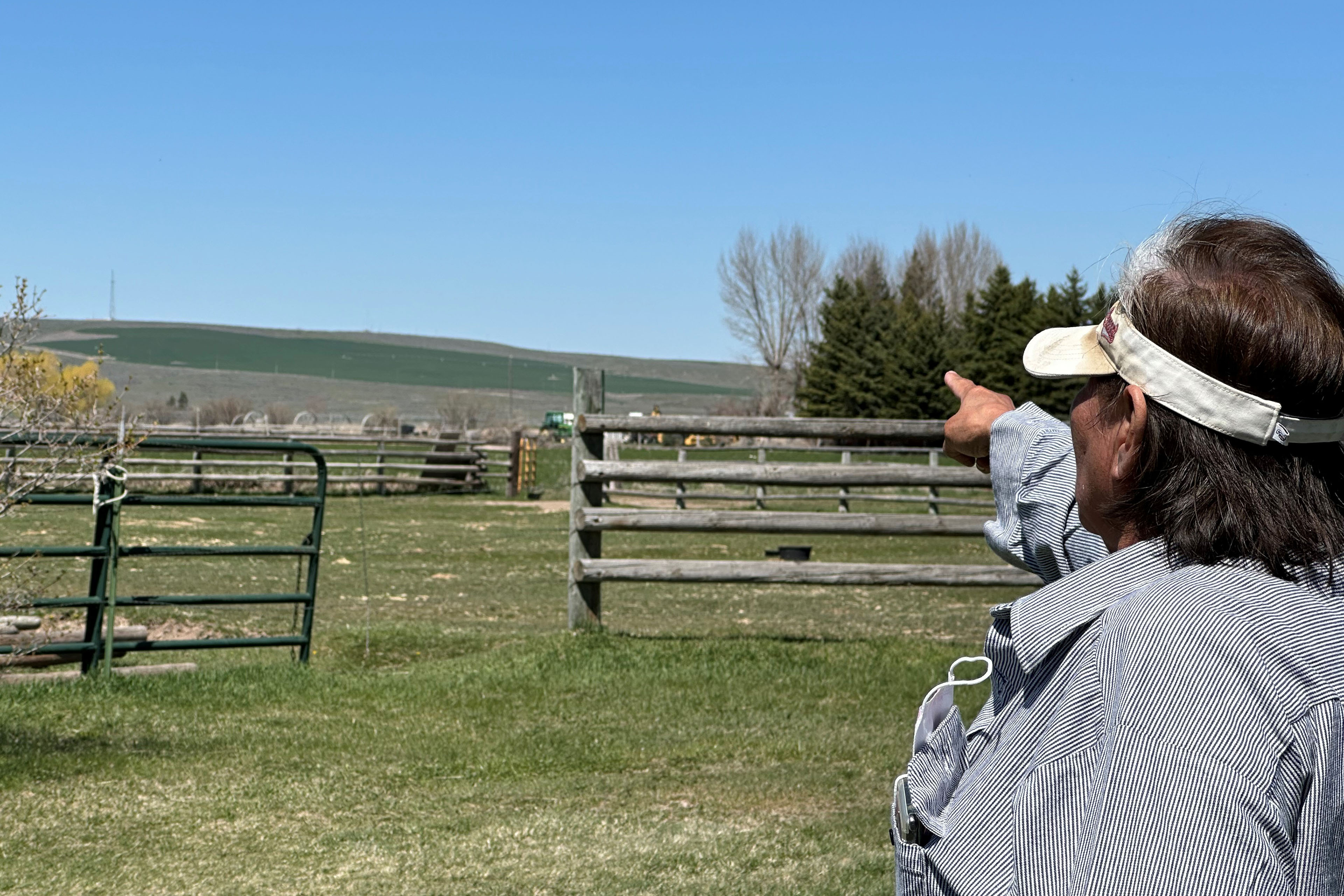 Myrna Broncho, who is standing outdoors beside a large, open field on a sunny day, points to a distant tower that connects her to an internet provider.