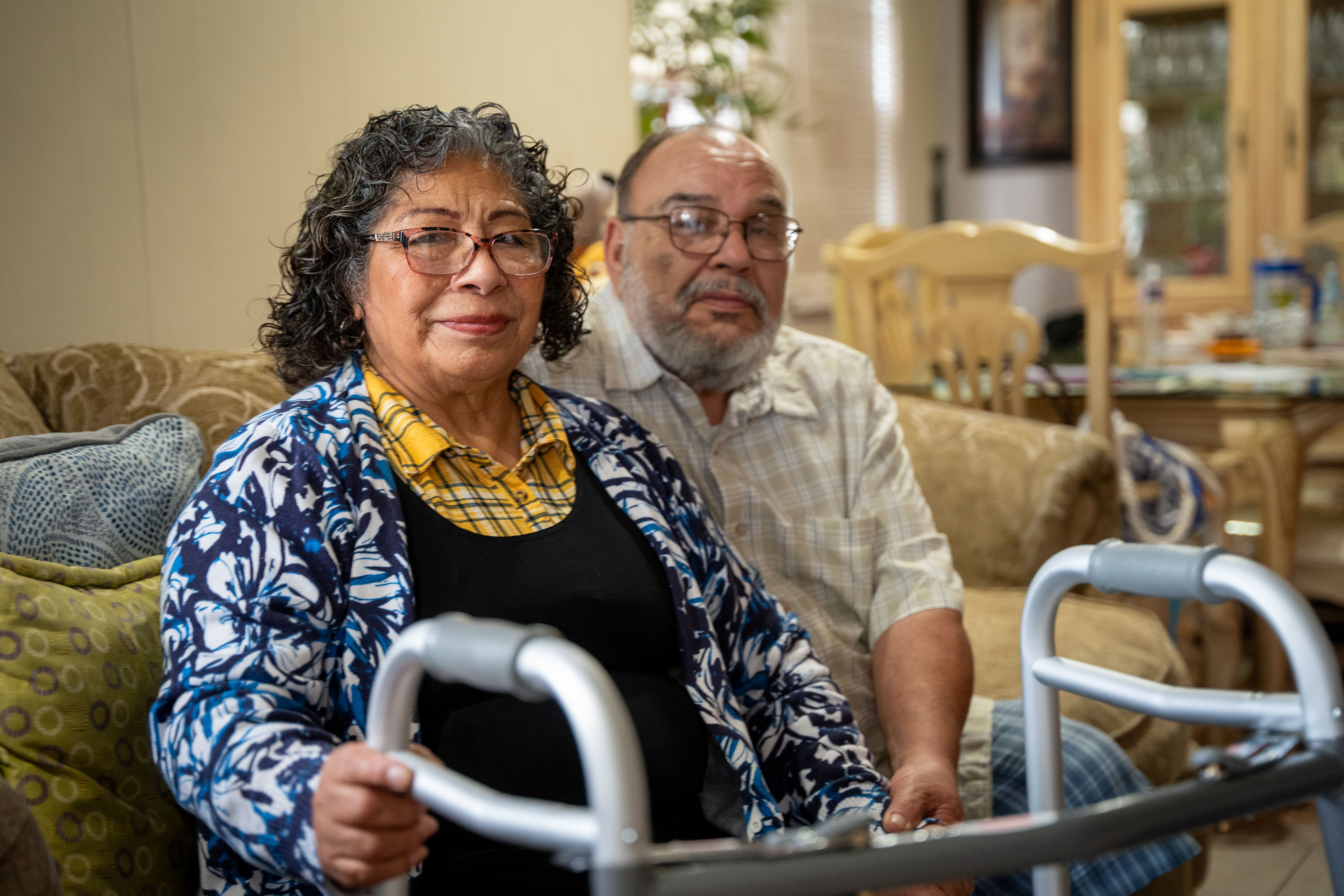 A woman sits next to a man on a couch. The woman holds a walker.