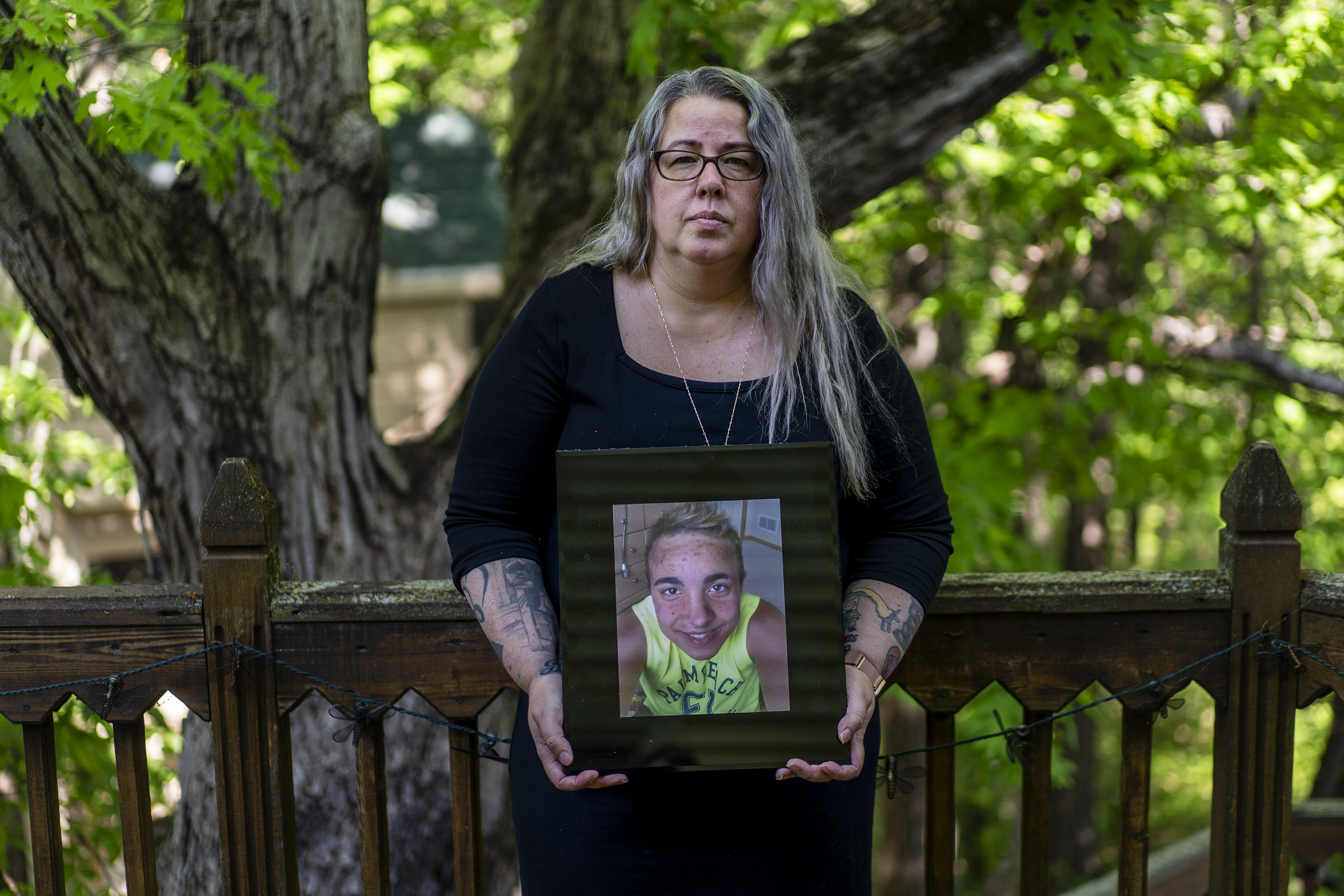 A portrait of a mother standing outside, holding a picture of her late son.