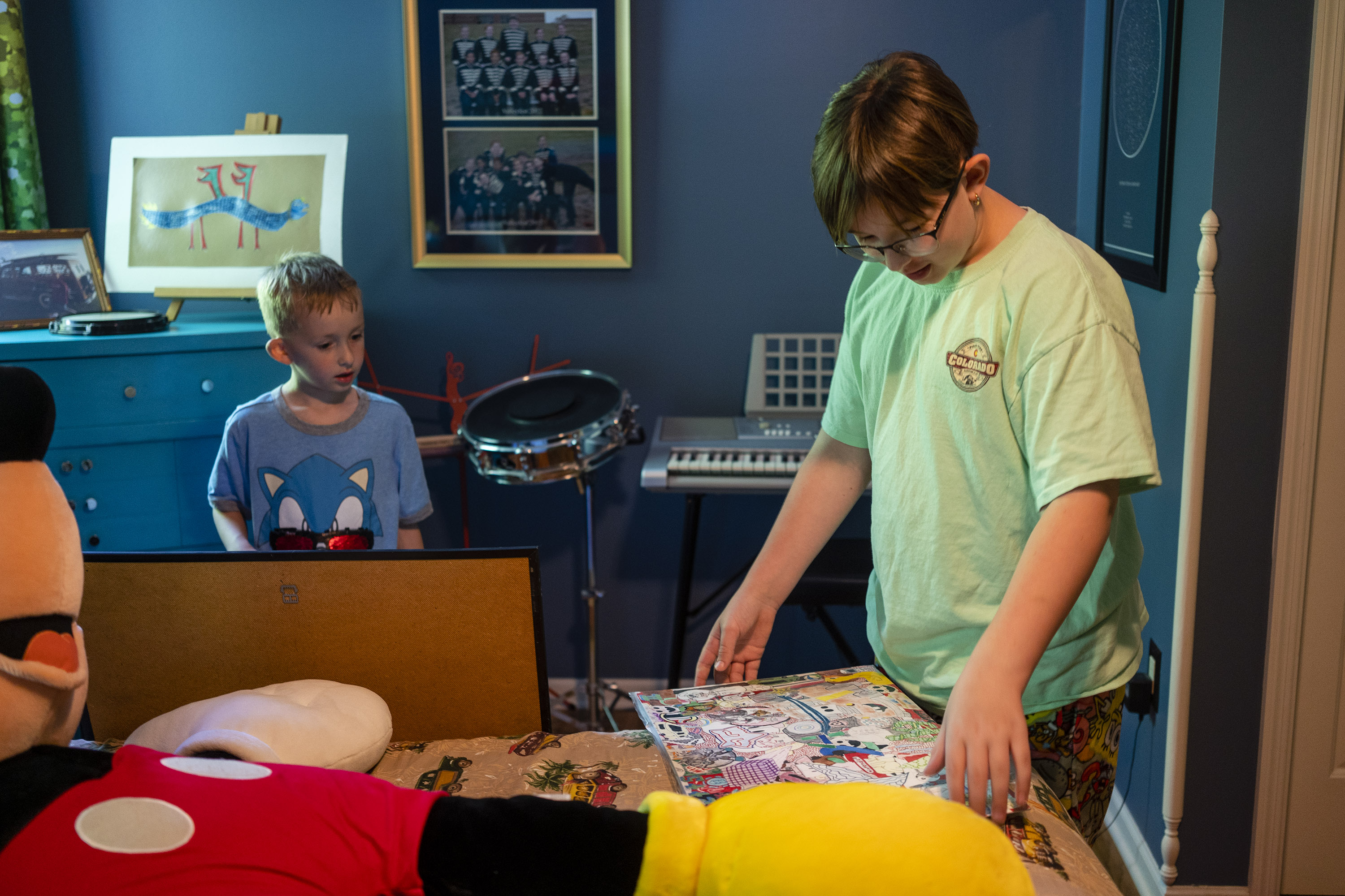 A photo of two young children looking at their late older brother's artwork in his room.